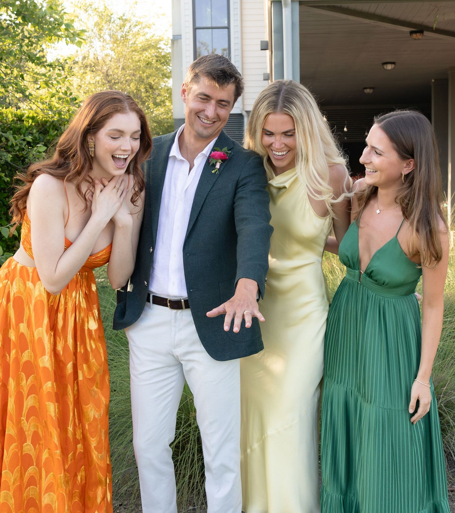 Four friends laughing and posing together at an outdoor wedding celebration in colorful formal attire.