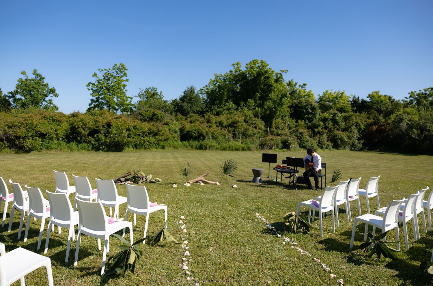 White chairs arranged in rows on green lawn for an outdoor wedding ceremony on a sunny day.