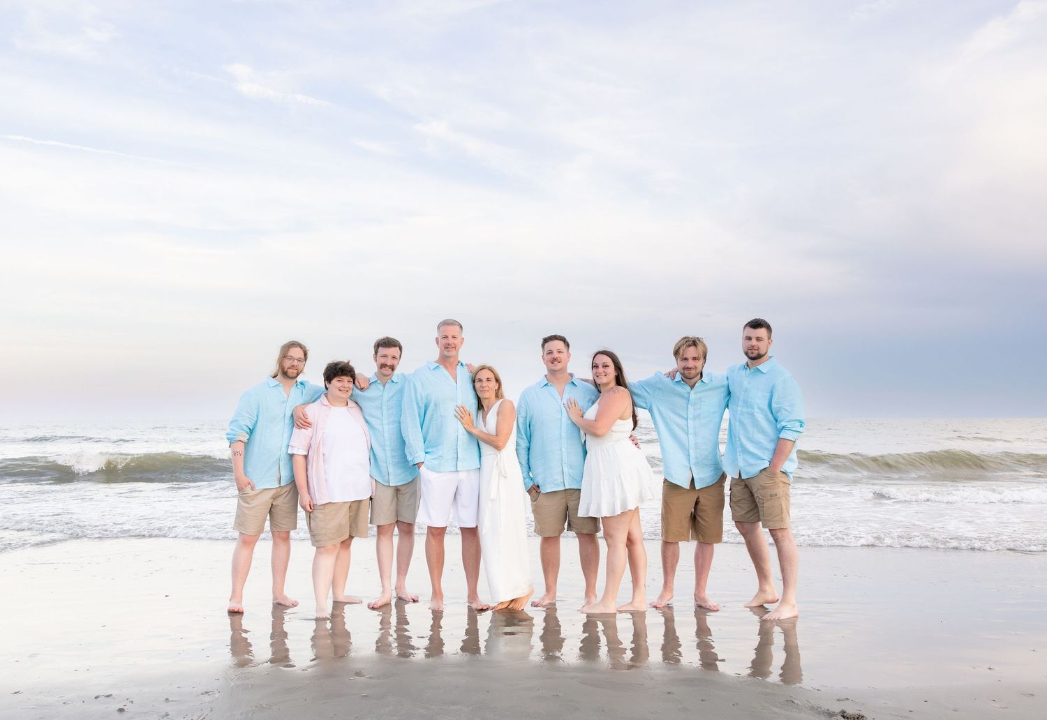 Group of family members posing together on a beach in coordinating blue shirts and khaki shorts.