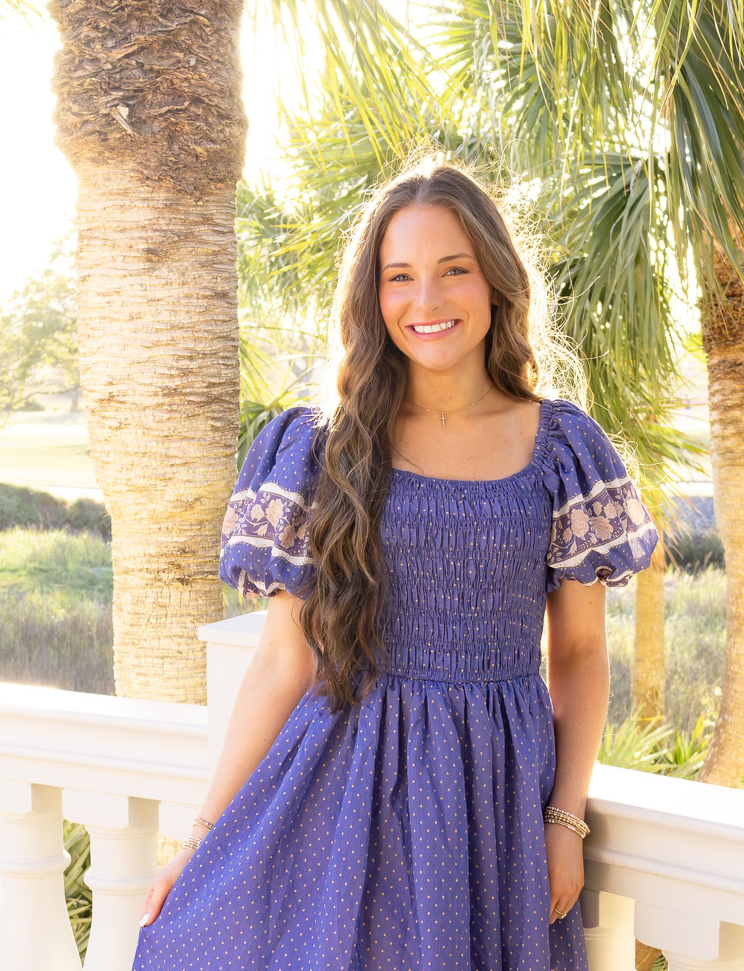 Woman in blue smocked dress with puff sleeves smiling outdoors near palm trees.