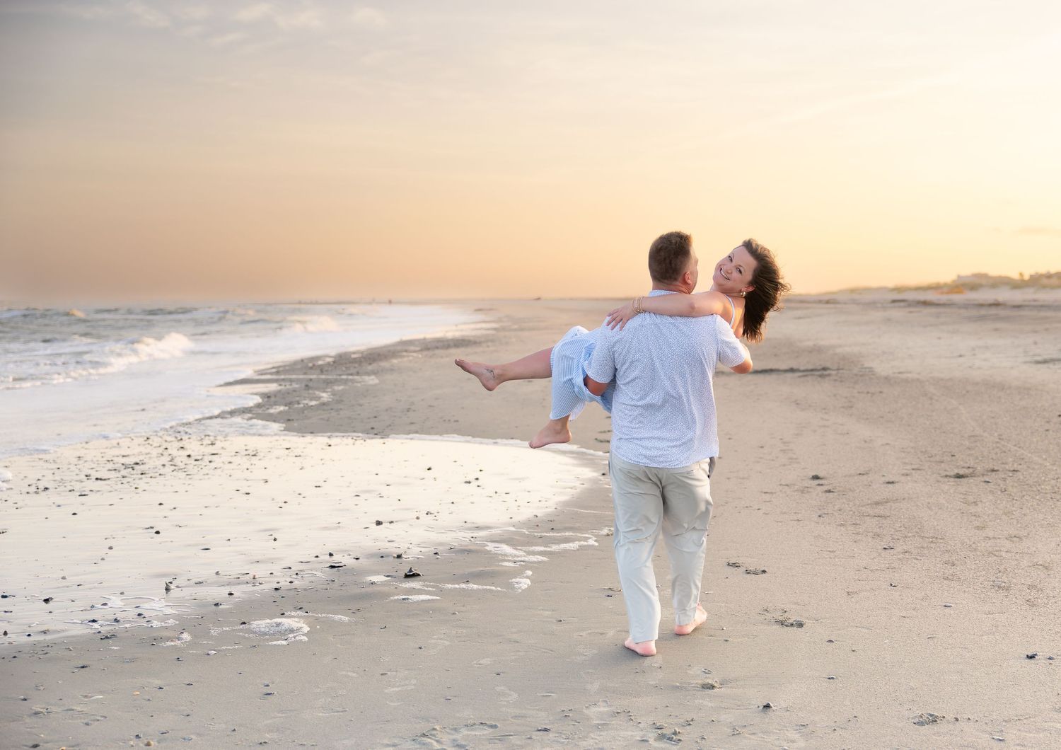 Couple sharing a romantic sunset moment on the beach, man carrying woman in his arms along the shoreline.