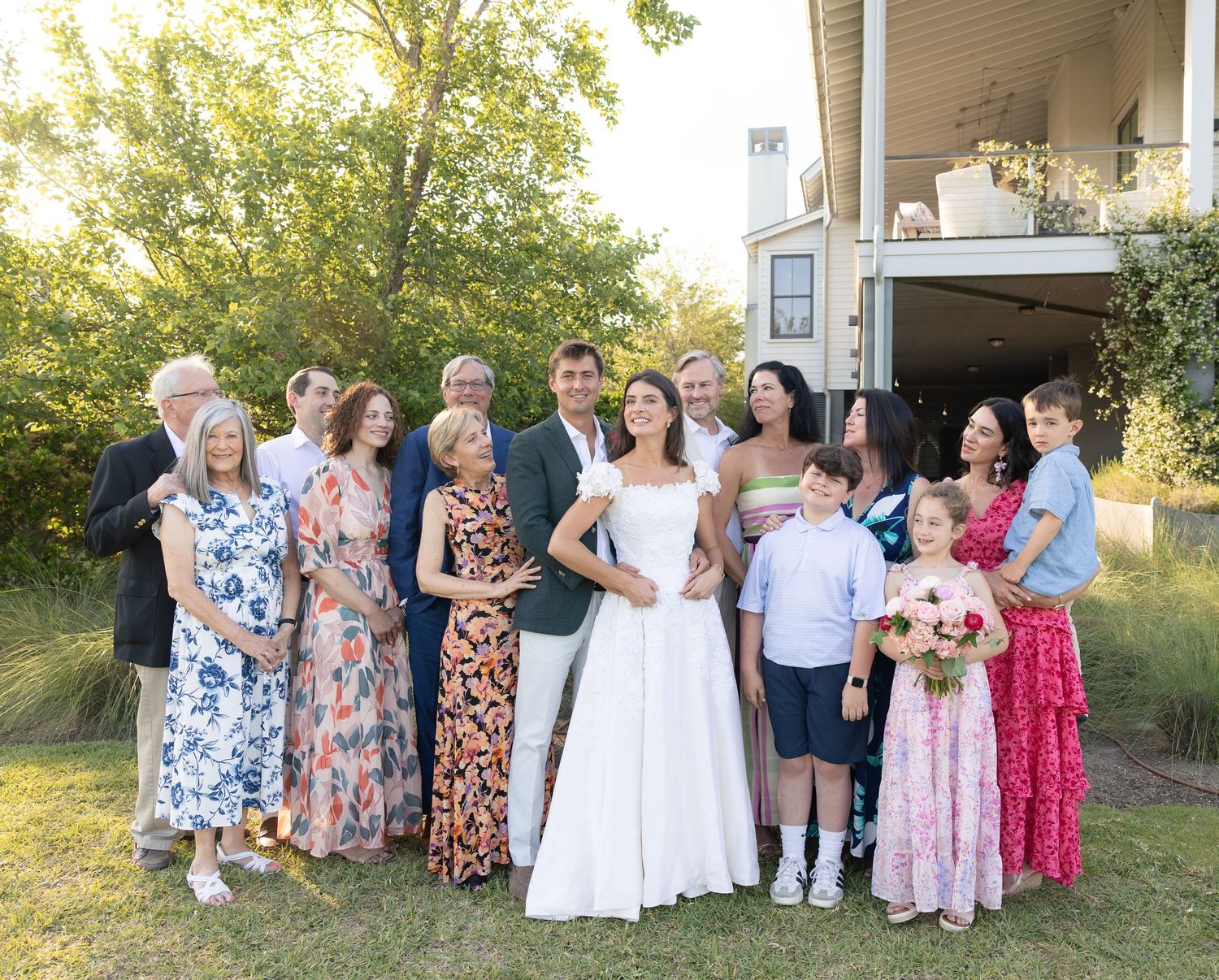 Large family group portrait with bride in white dress surrounded by guests of all ages at outdoor wedding reception.