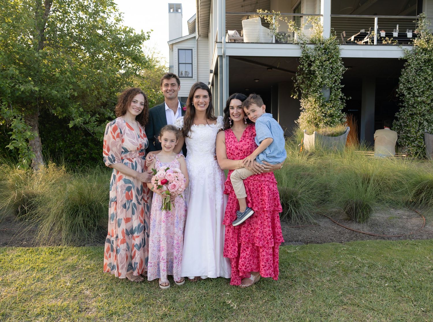 Family group portrait with bride in white dress posing outdoors at a backyard wedding venue.