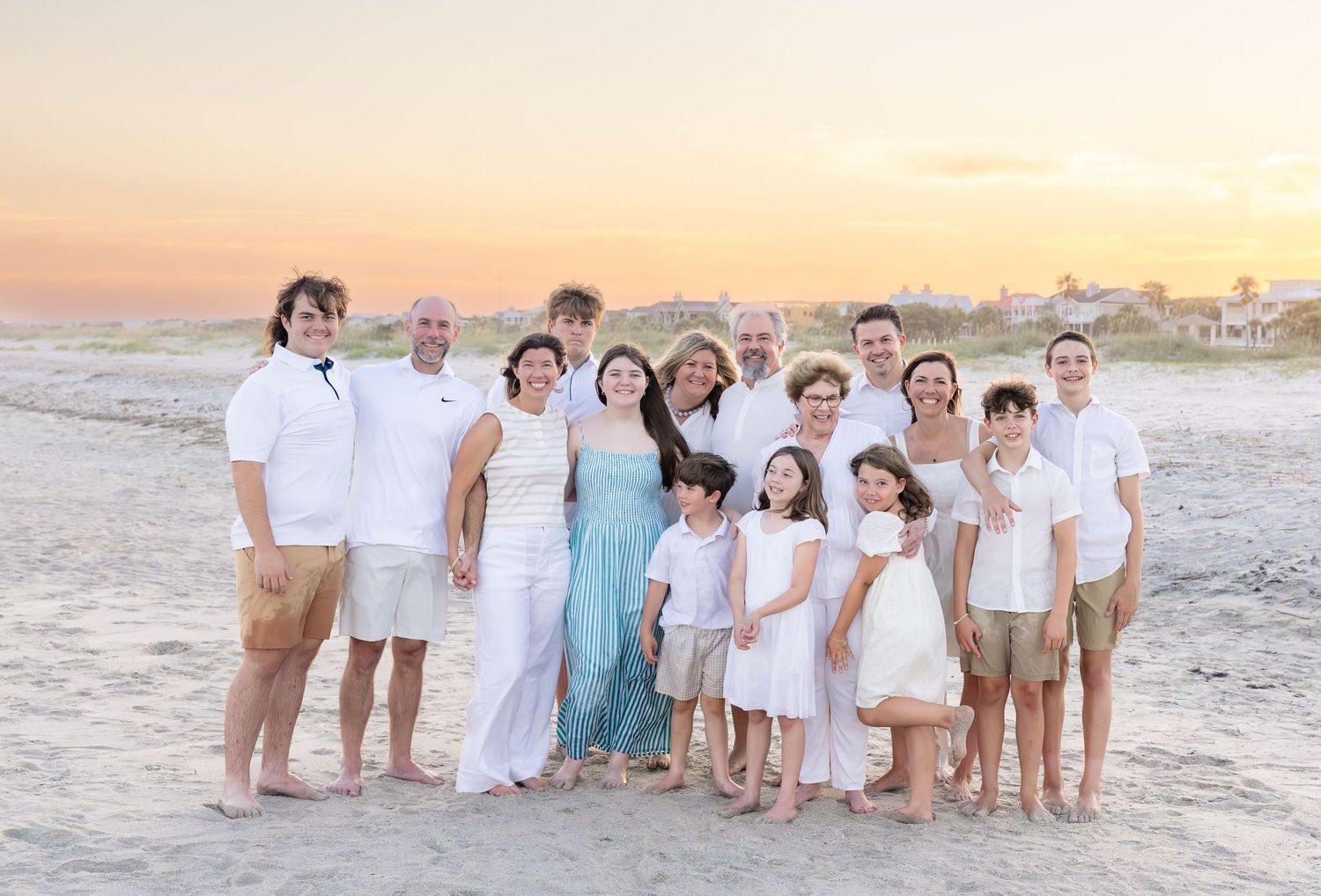 Large family group portrait on beach at sunset, wearing white and light blue coordinated outfits.