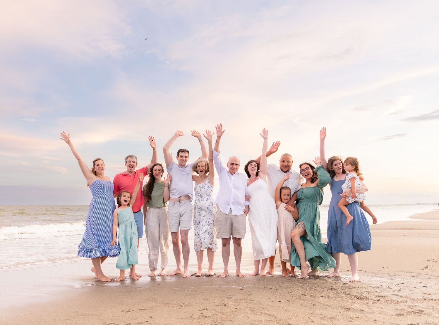 Large family group celebrating on a beach at sunset, waving arms joyfully in coordinated outfits.
