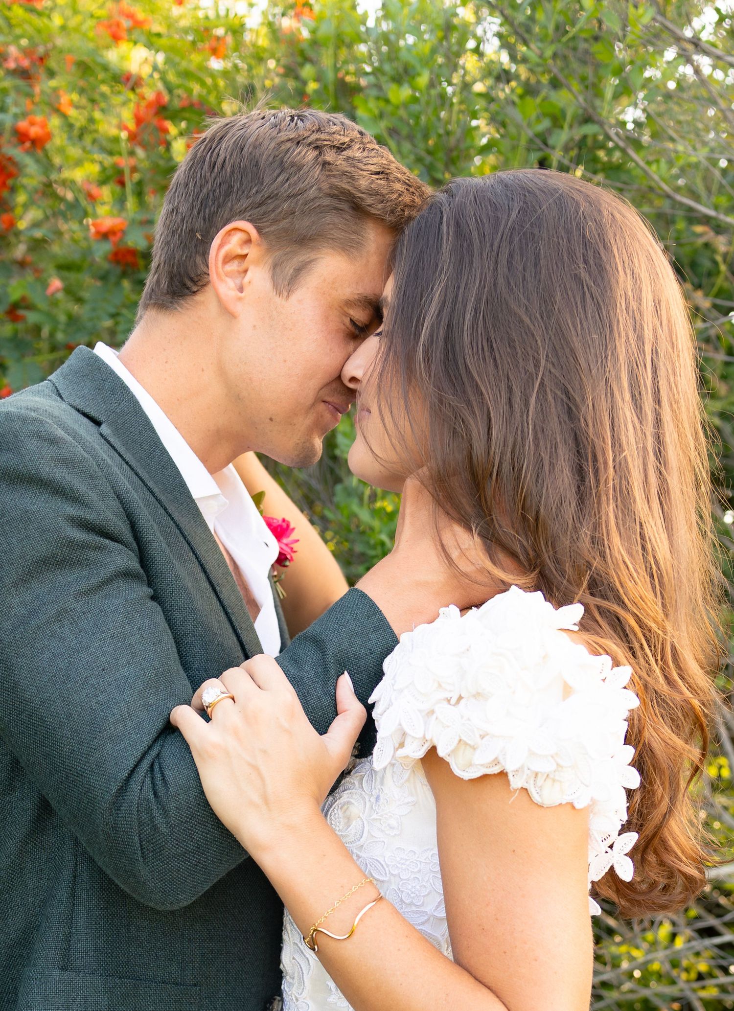 Bride and groom sharing romantic almost-kiss moment surrounded by colorful garden blooms.