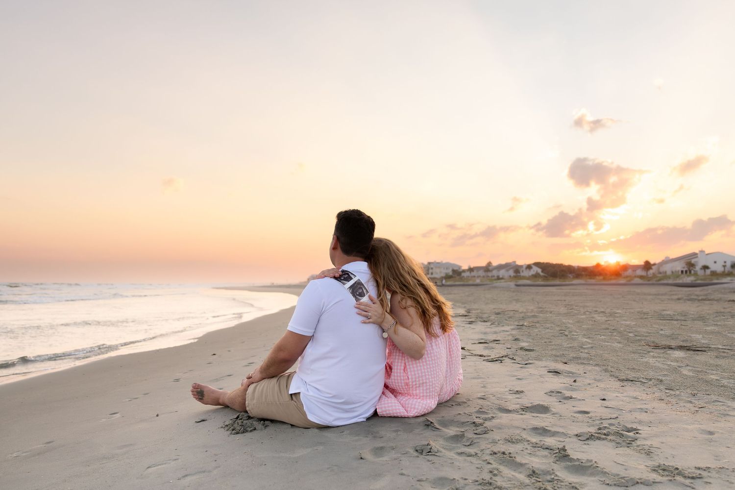 Couple sitting together on a sandy beach watching a beautiful sunset over the ocean.