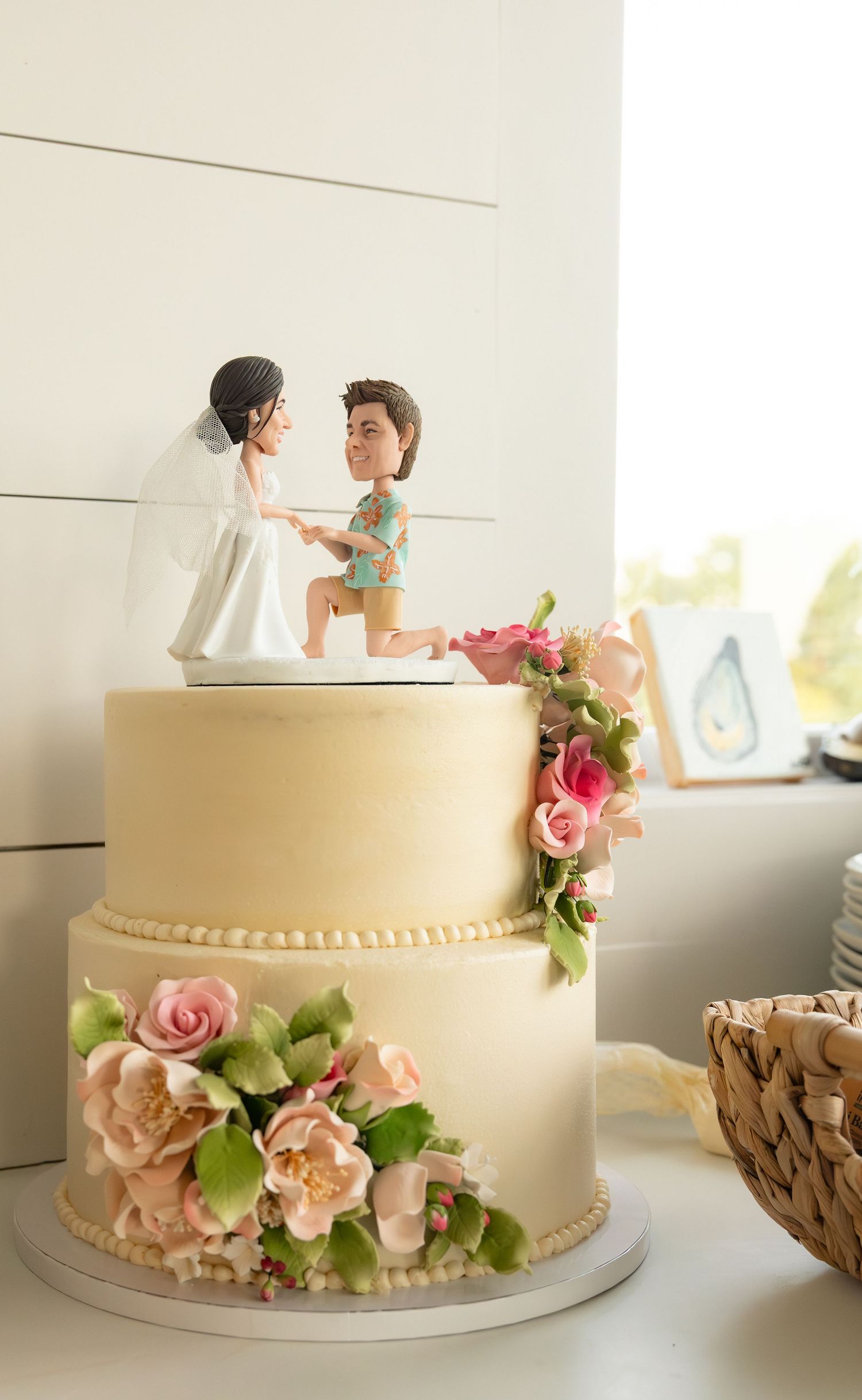 Two-tier wedding cake with floral decorations and custom bride and groom cake topper.