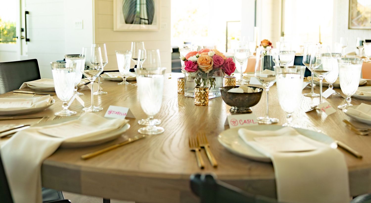 Rustic wooden wedding reception table with gold accents, white napkins, and vibrant floral arrangement.