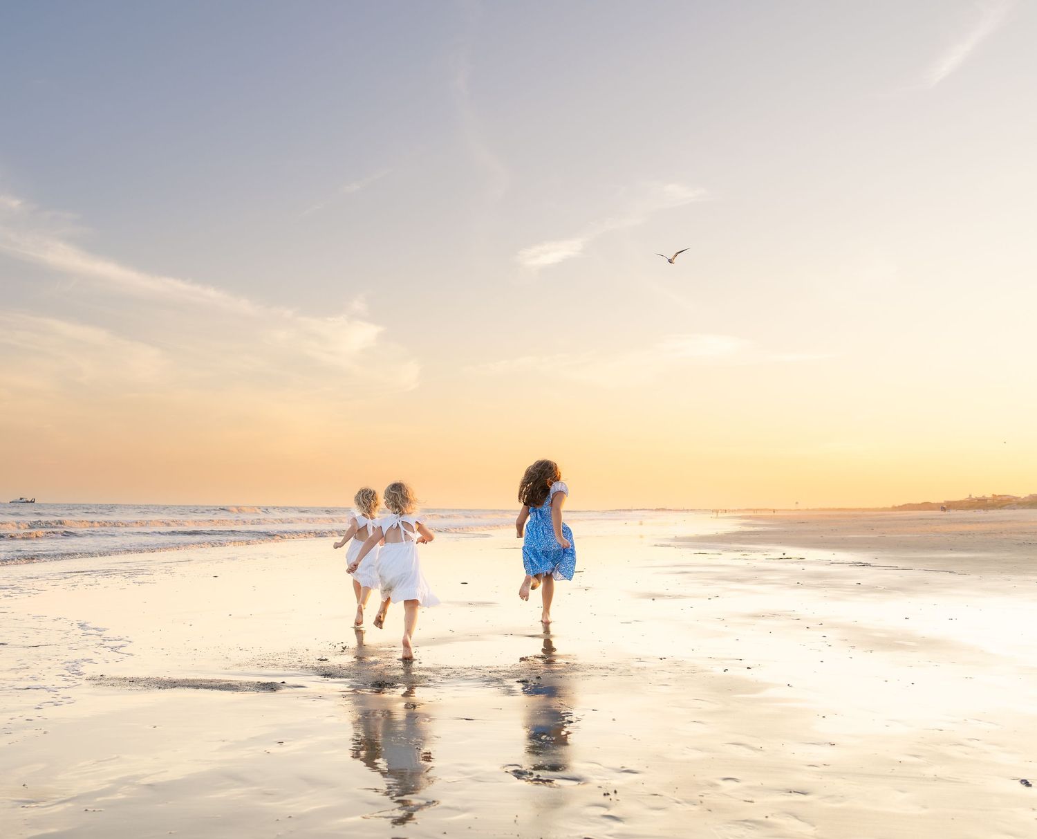 Three children running along a sandy beach at golden sunset, waves reflecting warm orange light on wet sand.