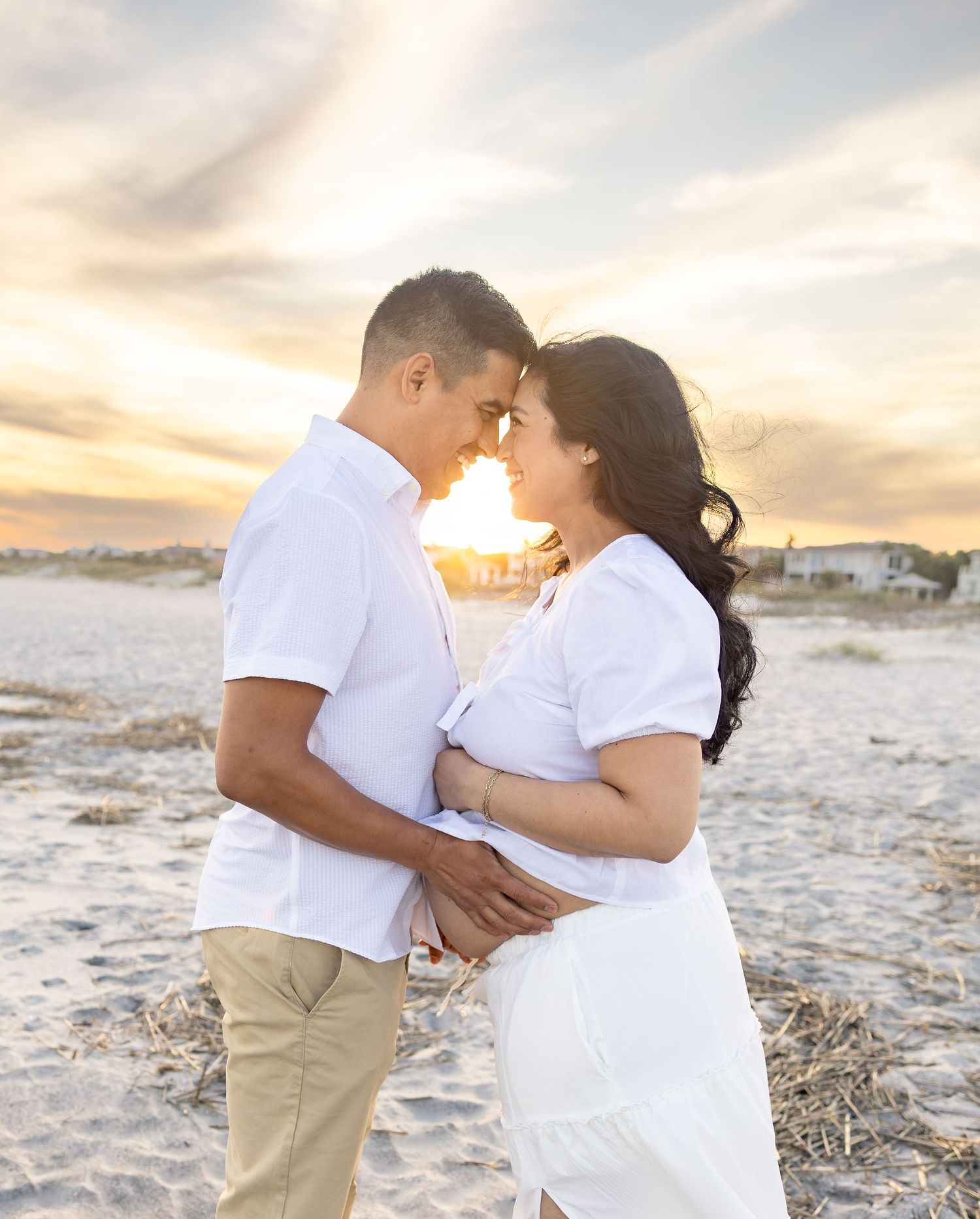 Couple in matching white outfits embracing on beach at golden sunset.