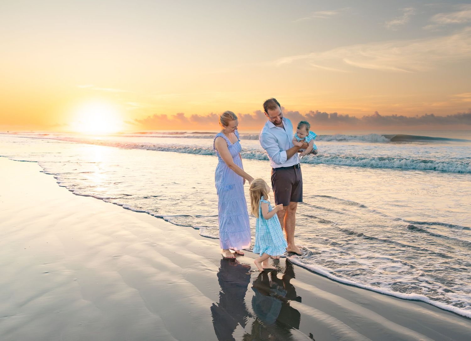 Family of four enjoying a beautiful golden sunset on a sandy beach with gentle ocean waves.