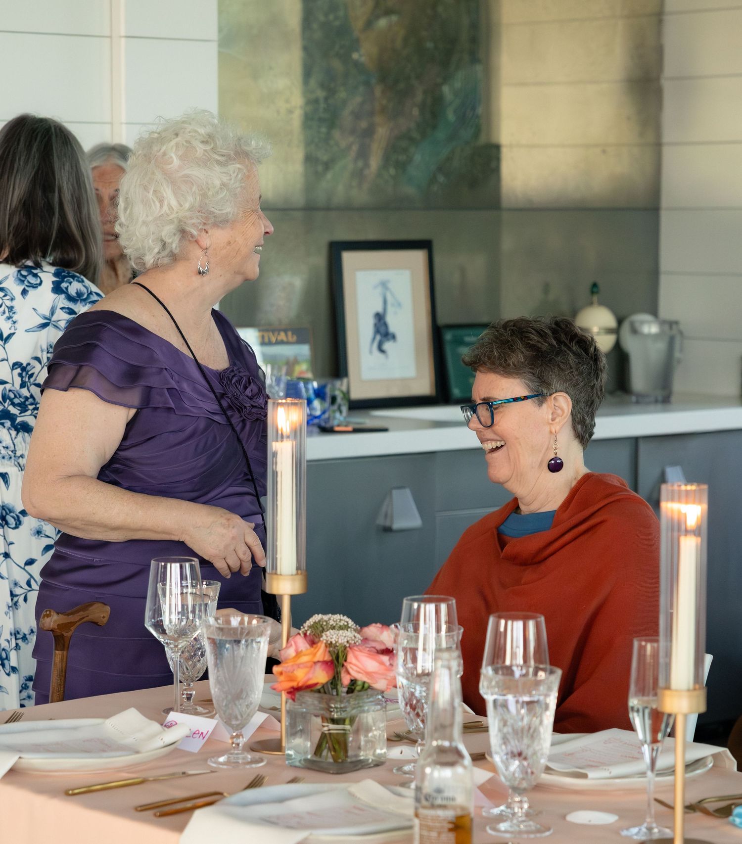 Two women conversing at elegantly set candlelit dinner table during wedding reception.