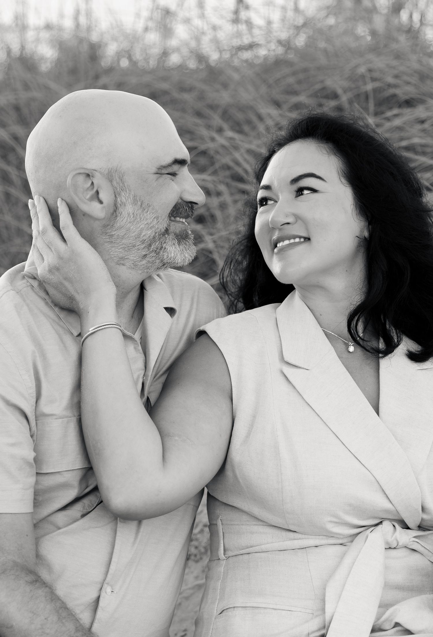 Black and white photo of a smiling couple sitting together outdoors, man with beard and woman with dark hair.