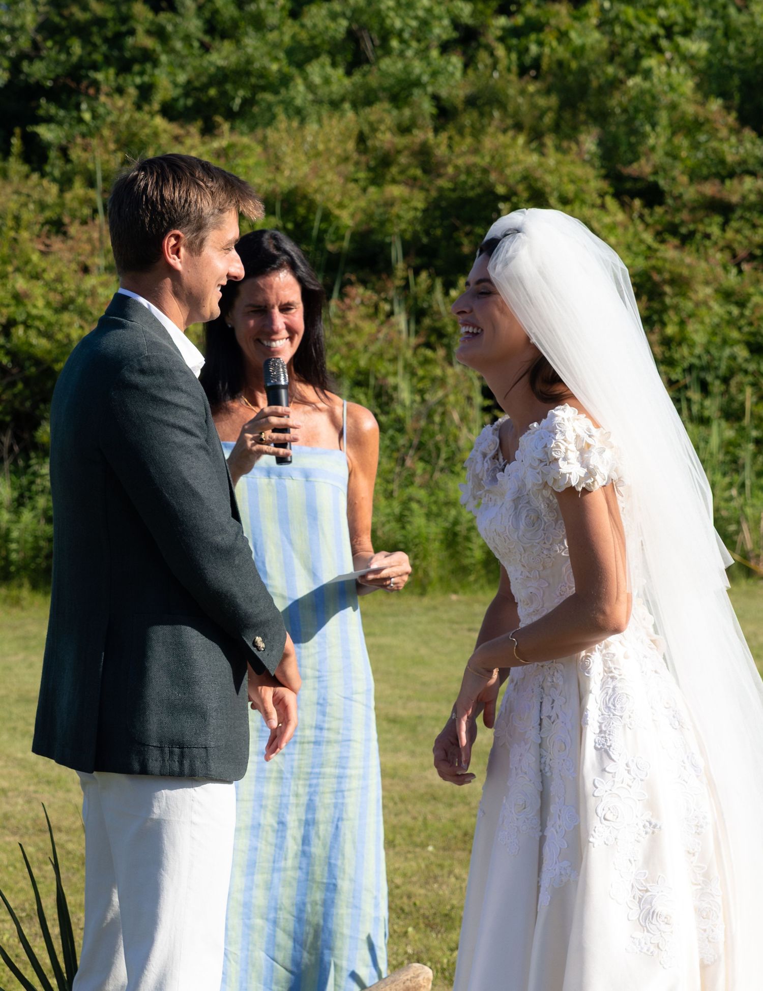Bride and groom exchange vows at outdoor wedding ceremony with female officiant in blue striped dress.