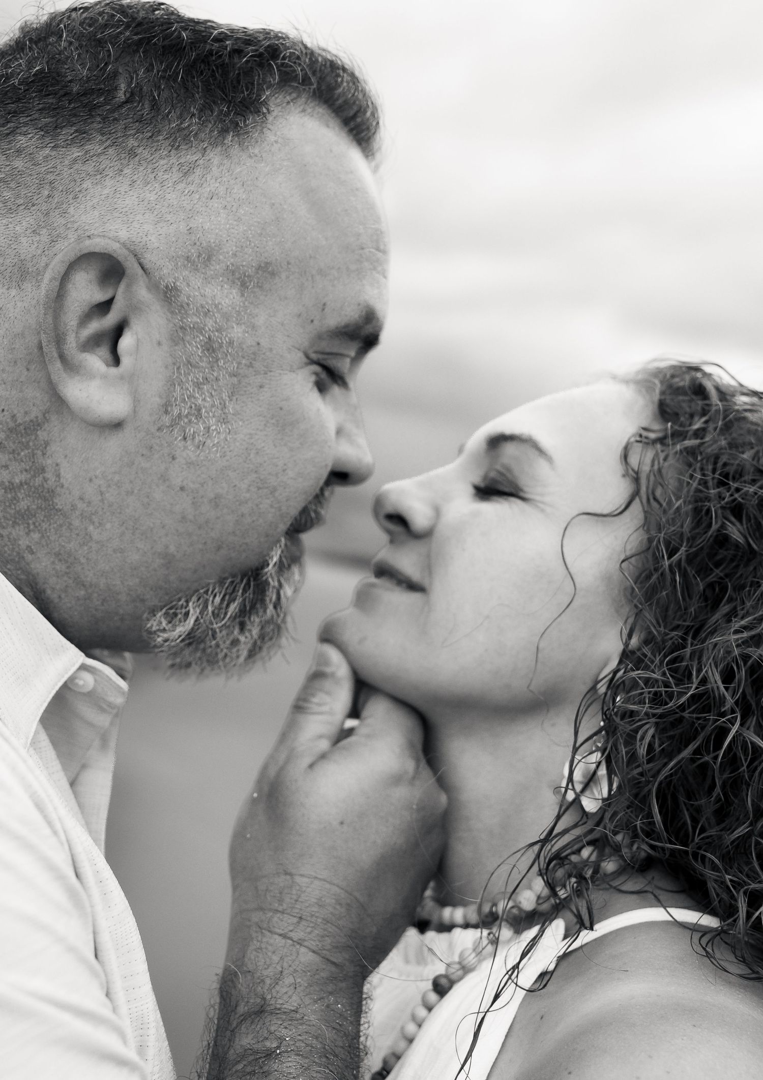 Black and white photo of a couple sharing a romantic moment, man gently holding womans chin as they lean in for a kiss.