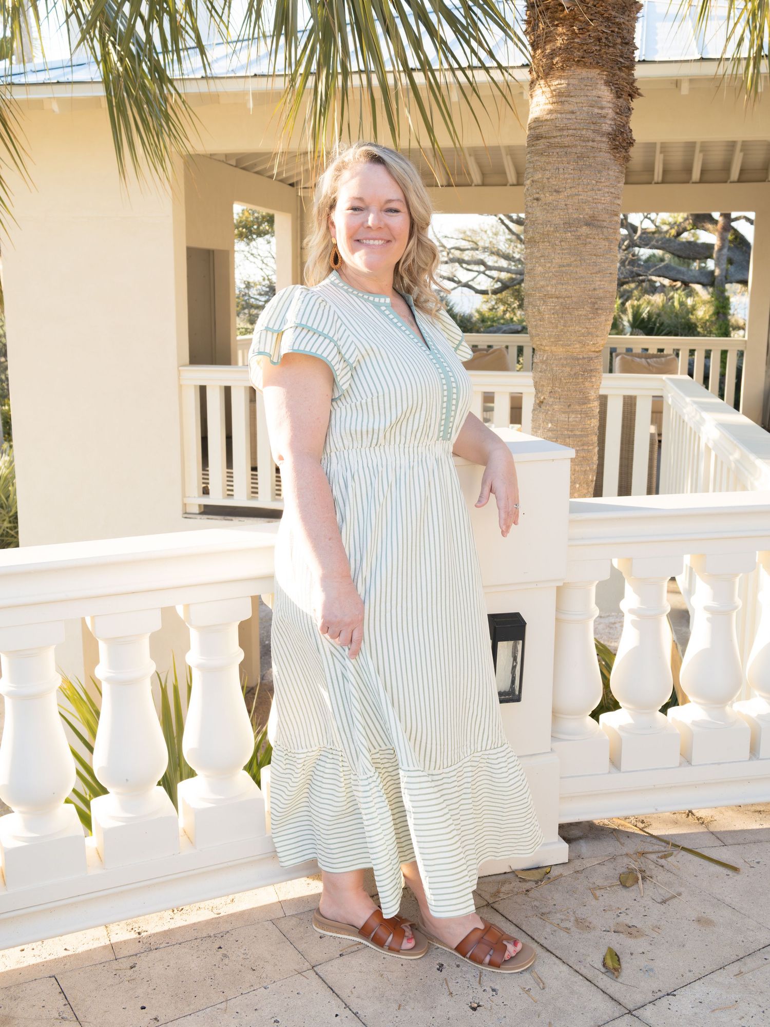 A smiling woman in a striped dress stands on a patio with palm trees in the background.