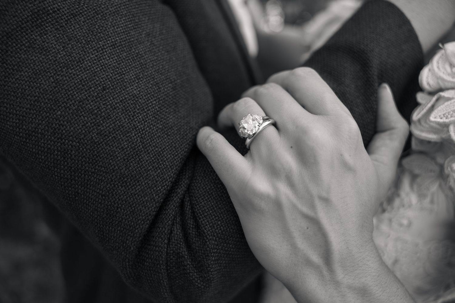 Close-up black and white photo of a bride wearing a stunning diamond engagement ring while holding groom's arm.