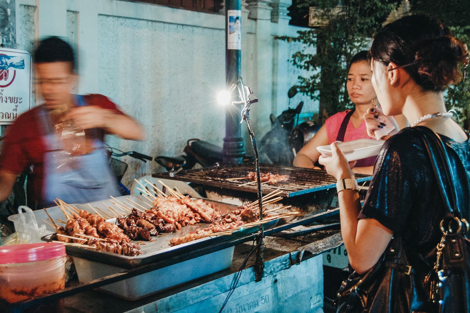 Street food vendor grilling meat at an outdoor market stall.