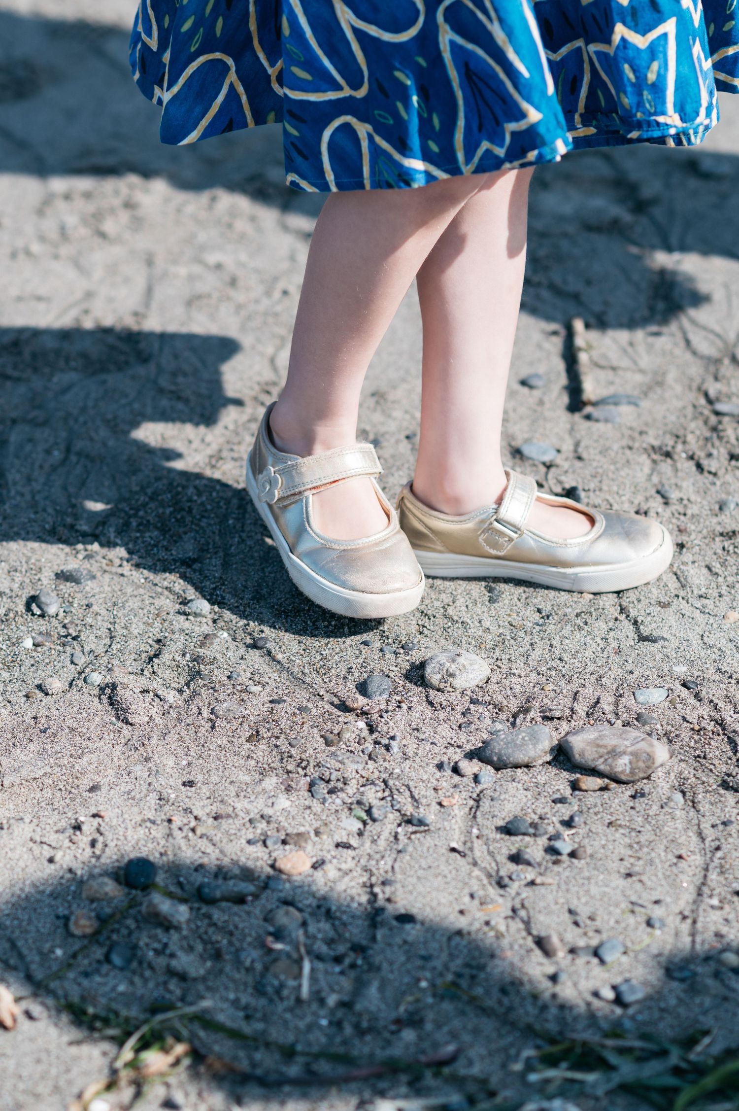 Close-up of white shoes on rocky beach ground.