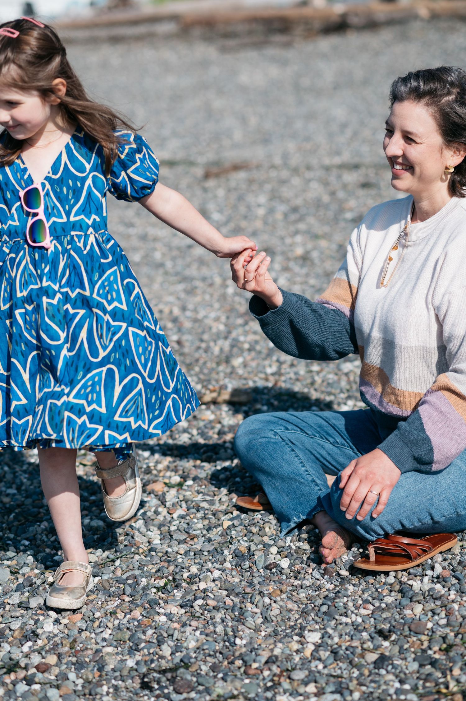 A person in a blue patterned dress plays on a rocky beach while another sits nearby.