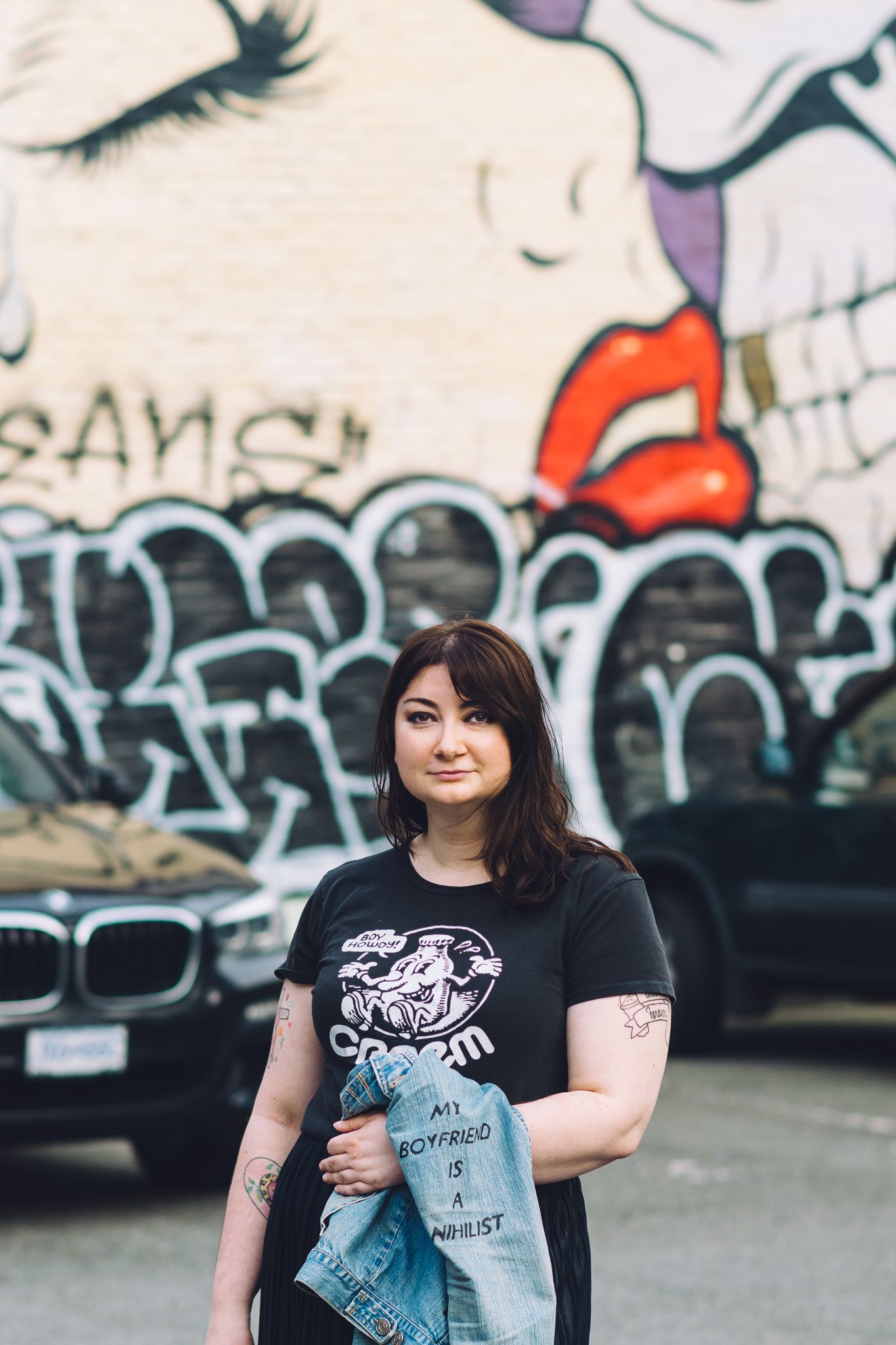 Person in black t-shirt poses against graffiti wall in urban setting.