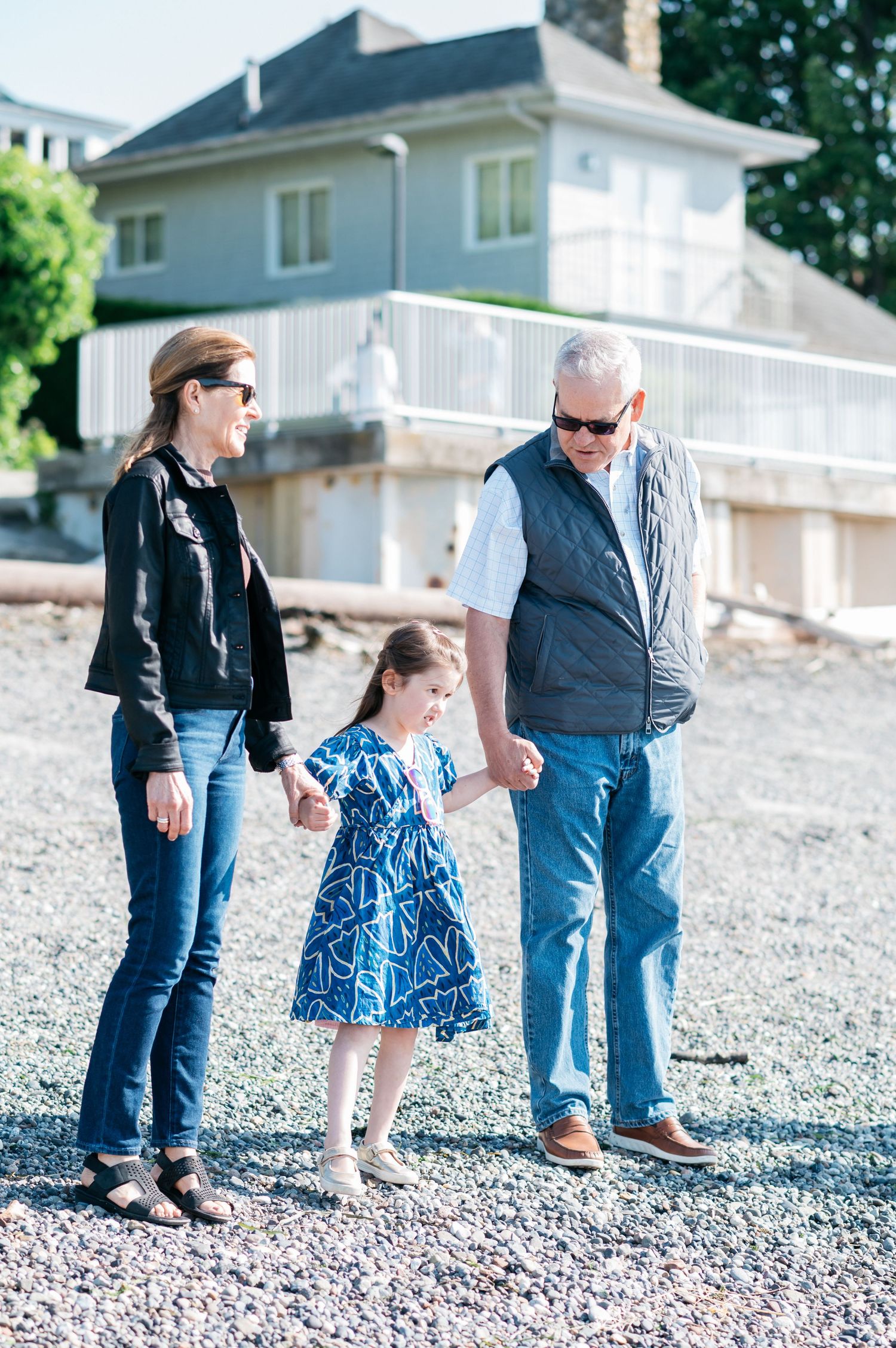 Family members in casual attire stand together on a pebbly beach.