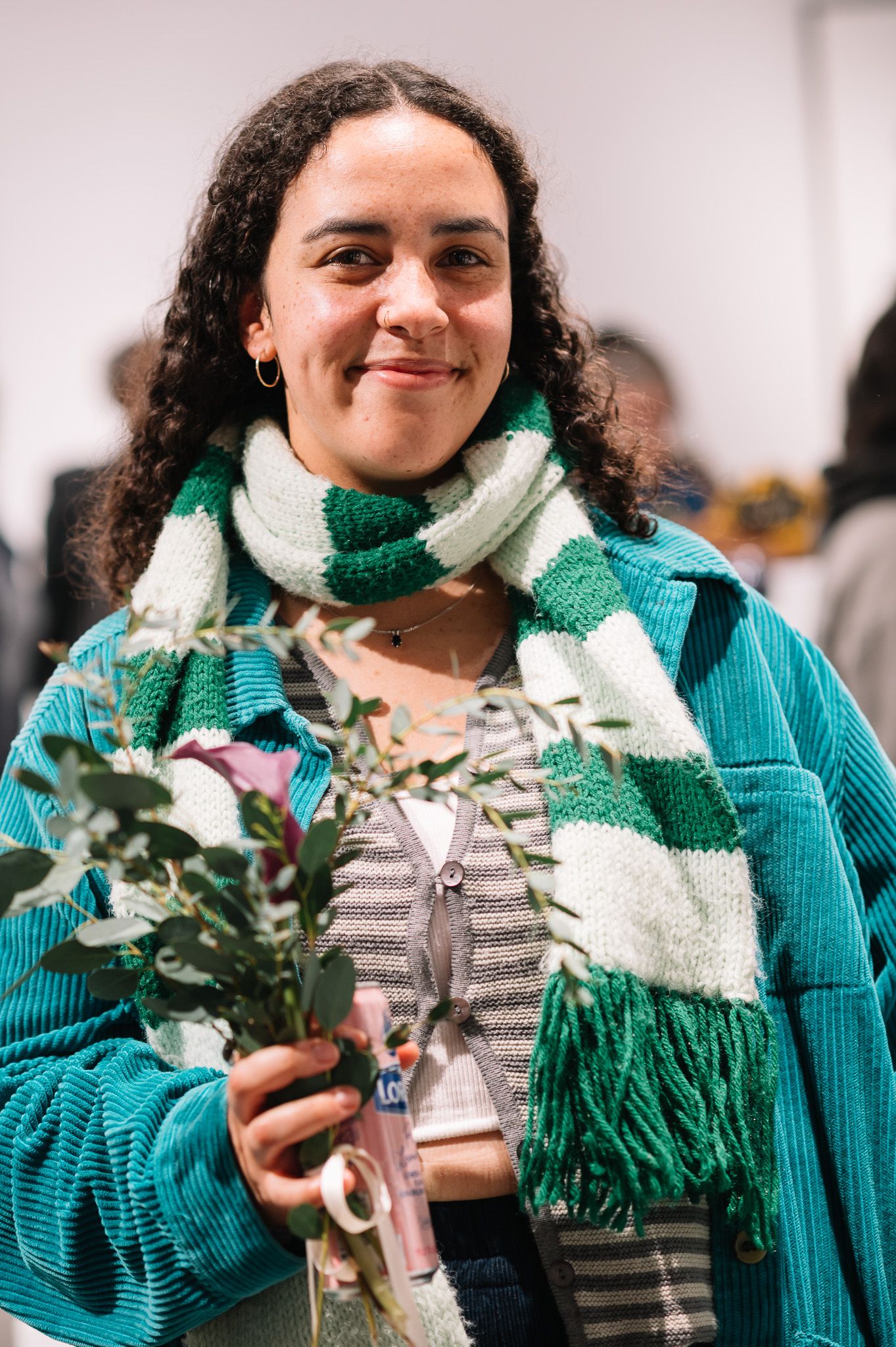 Person wearing a turquoise sweater and striped scarf holding decorative items.