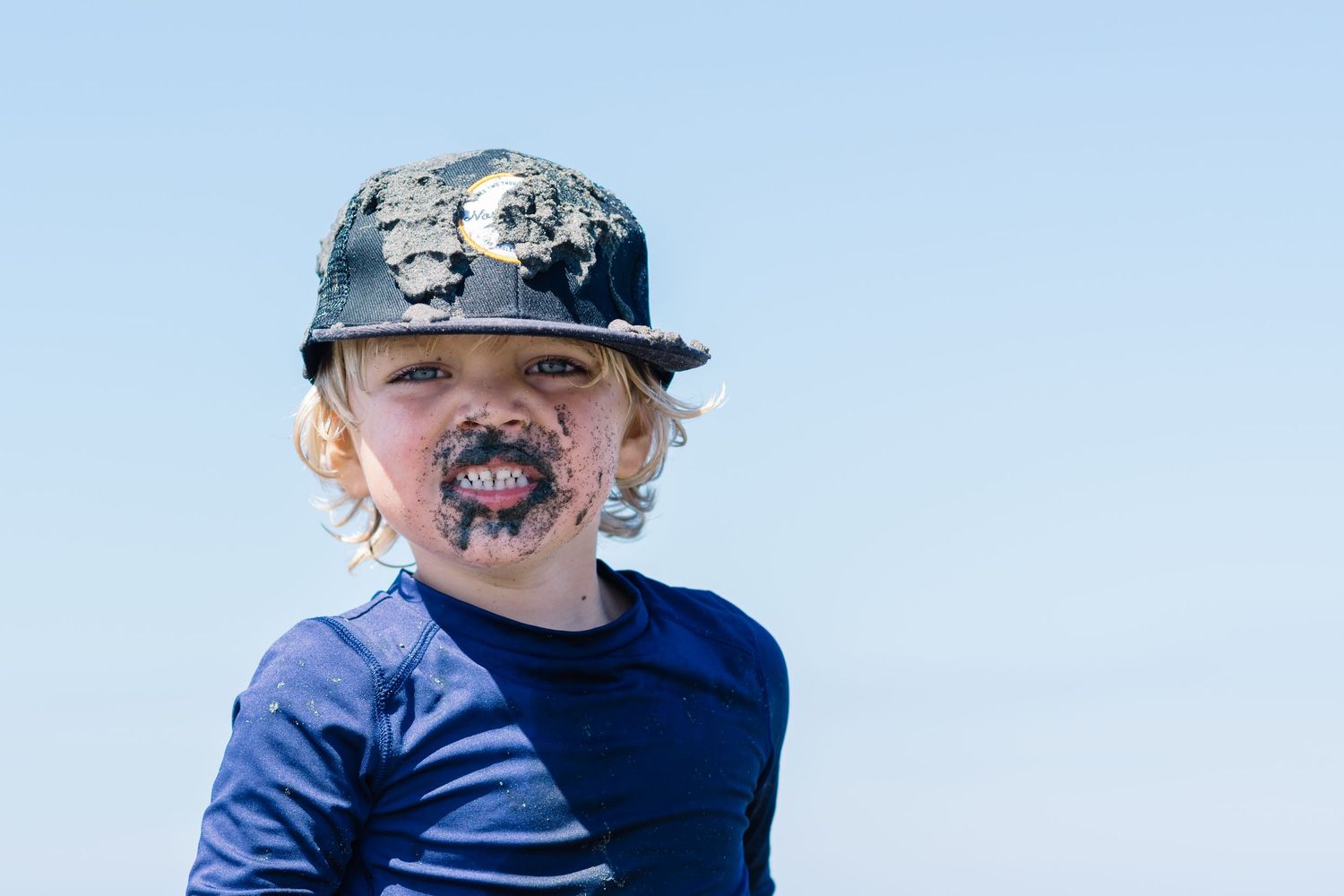 A small child wearing a blue shirt and patterned baseball cap with chocolate or ice cream smeared around their mouth.