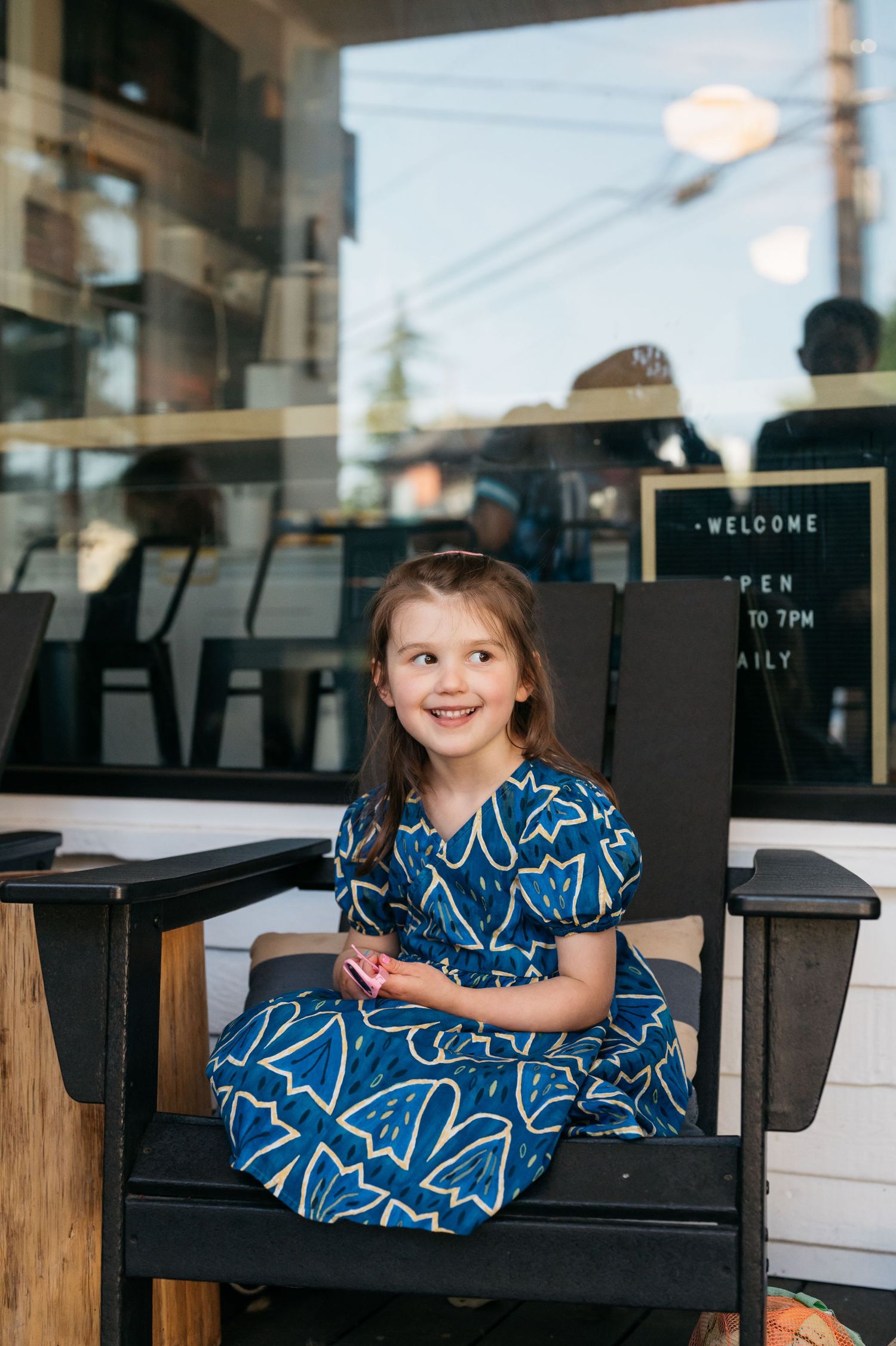 A child in a blue patterned dress sits on a black outdoor bench.