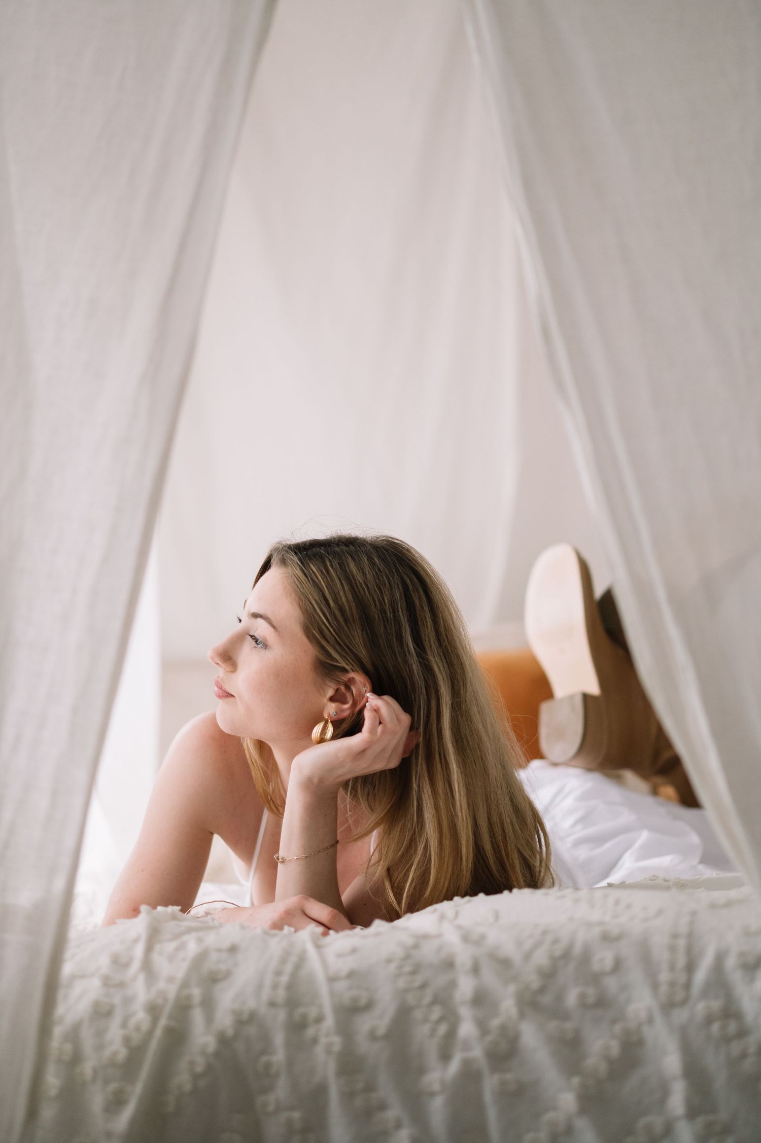 Dreamy boudoir photos showing person reclining on white bedding in soft natural light.