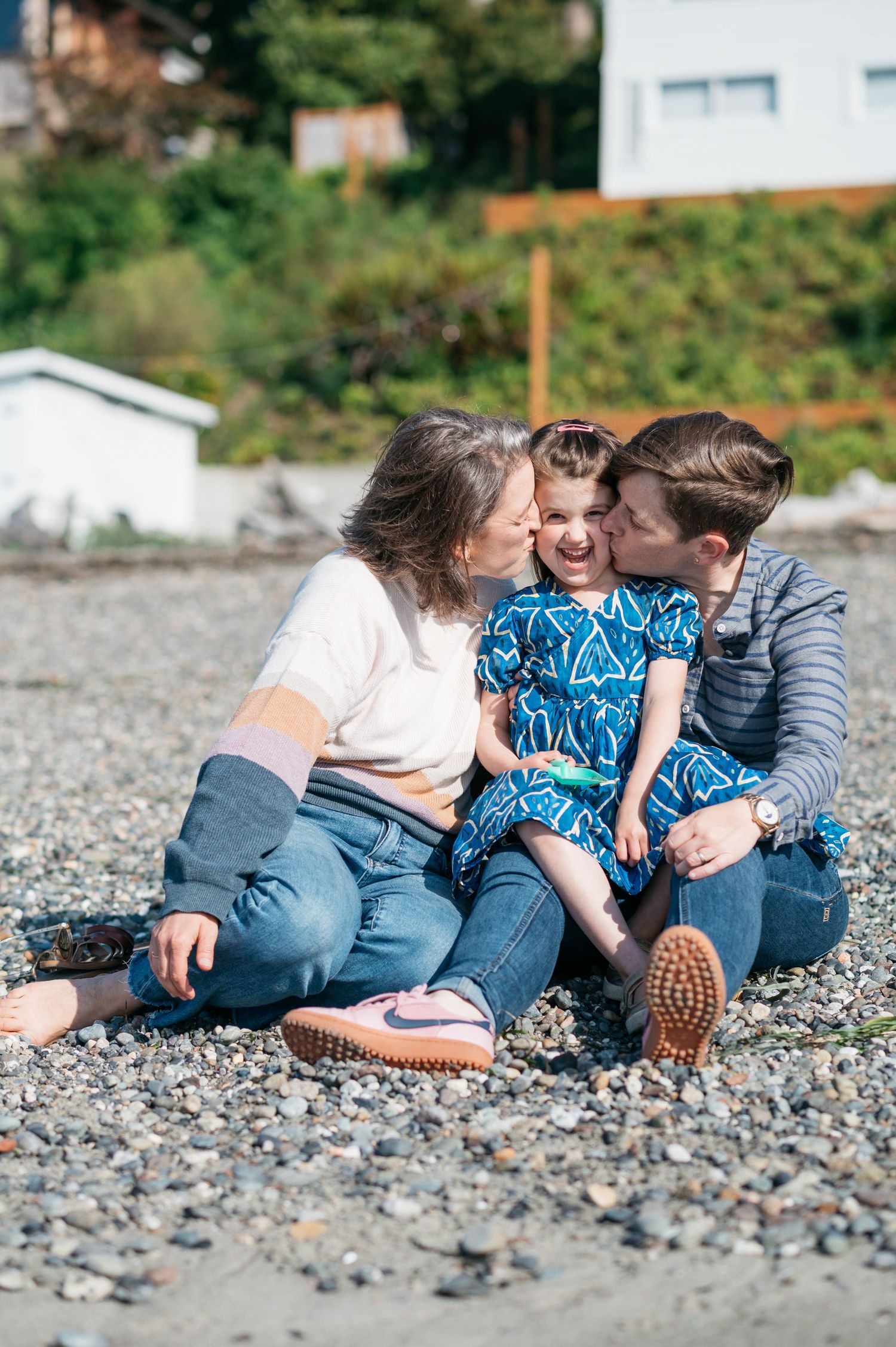 A family sharing a tender moment while sitting on a pebbly beach.