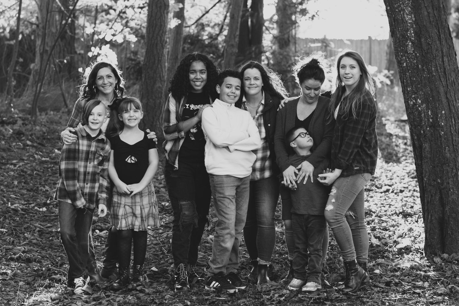 A diverse group of friends pose together for a casual photo in a wooded outdoor setting.