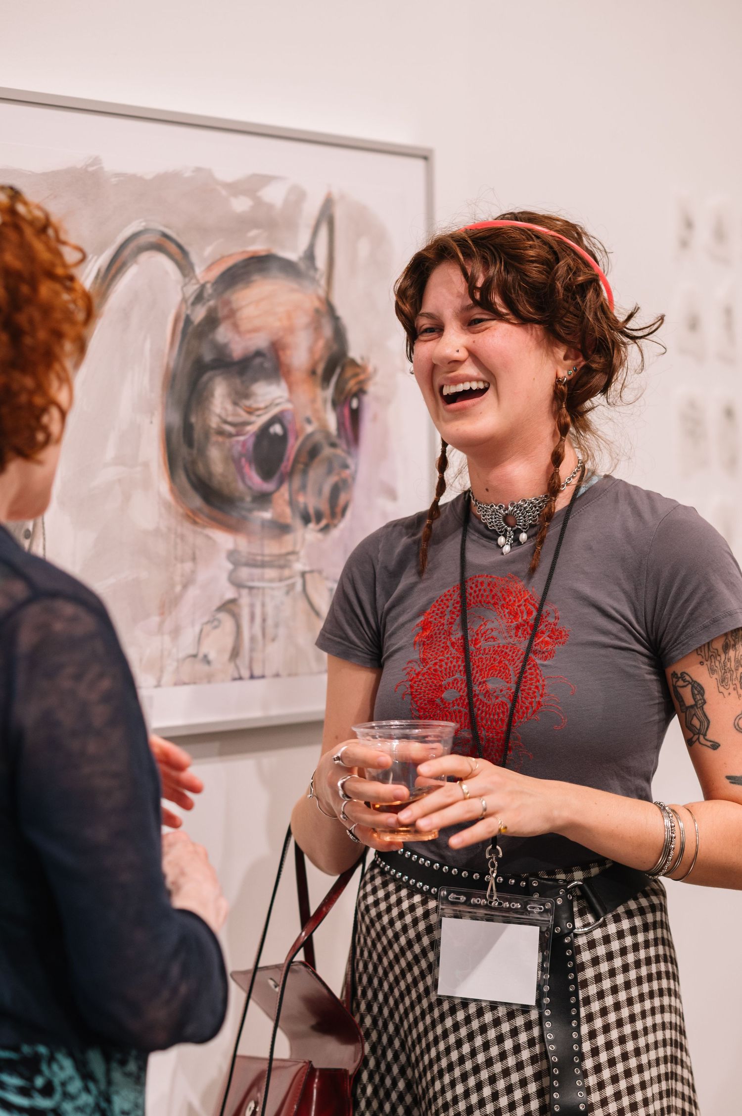A person in checkered pants and grey shirt laughs while attending an art gallery event.