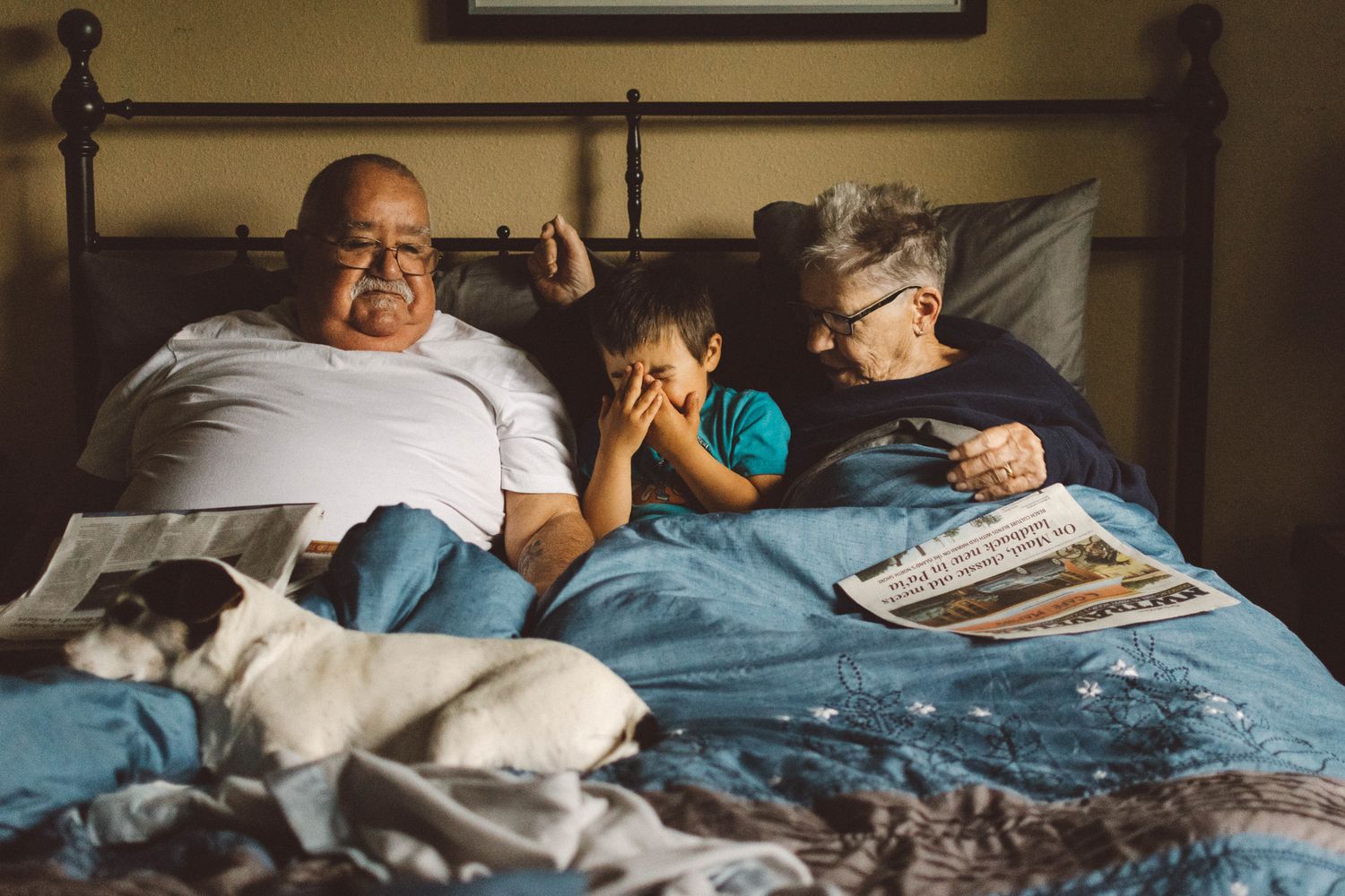 People relaxing together on bed while reading newspapers in dim lighting.