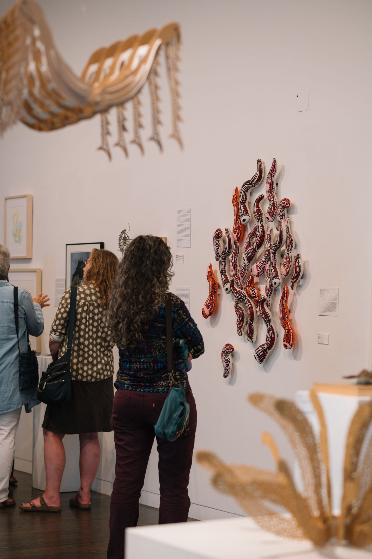Gallery visitors examine hanging textile art installations in a museum exhibition space.