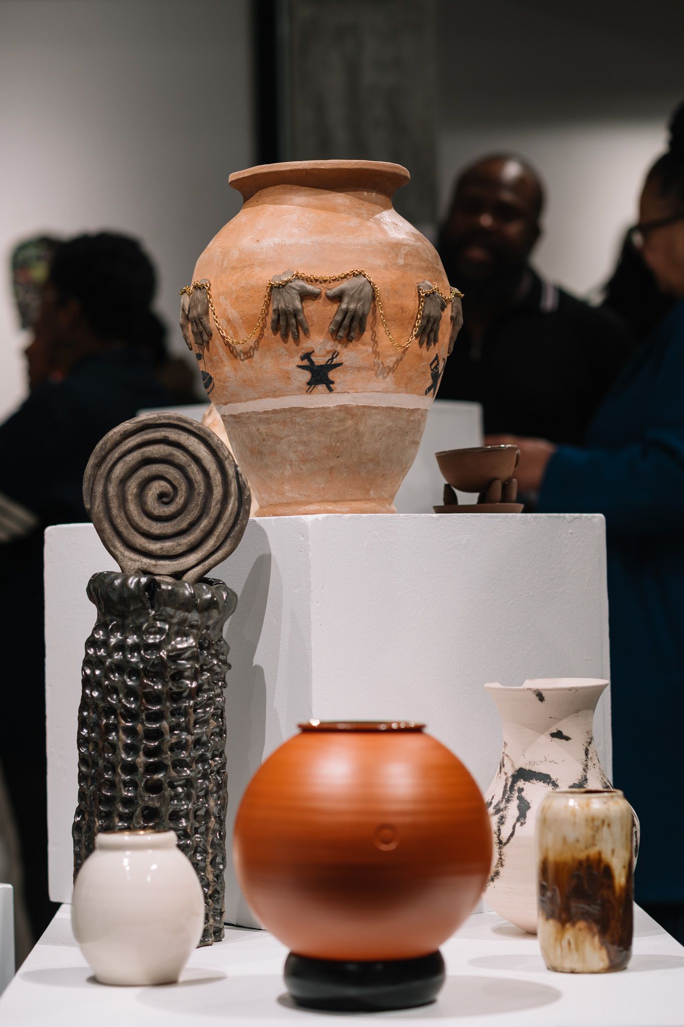 Collection of ancient ceramic pottery and vessels with spiral designs displayed on white pedestals.