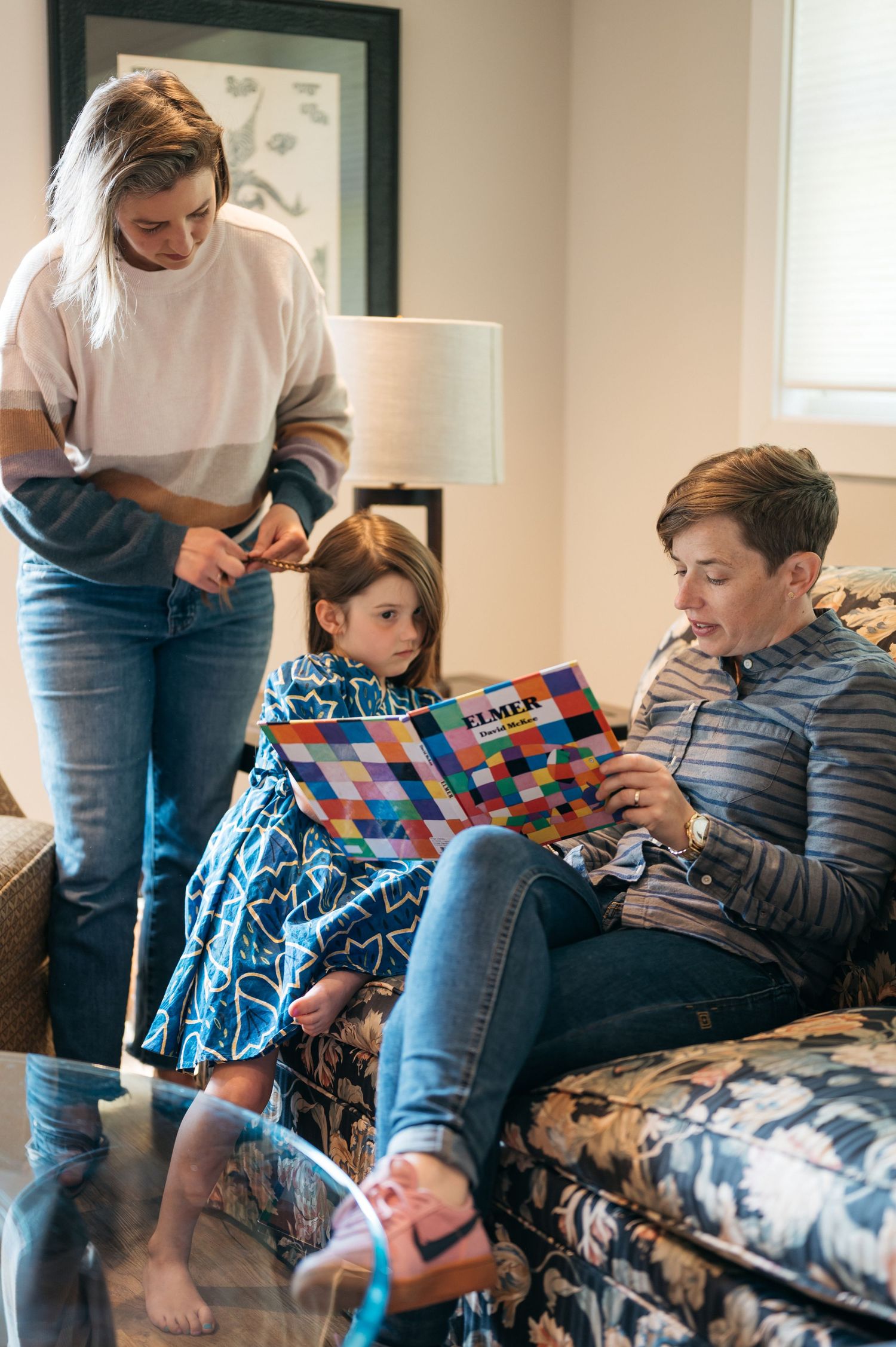 People looking at a colorful book while relaxing on patterned furniture.