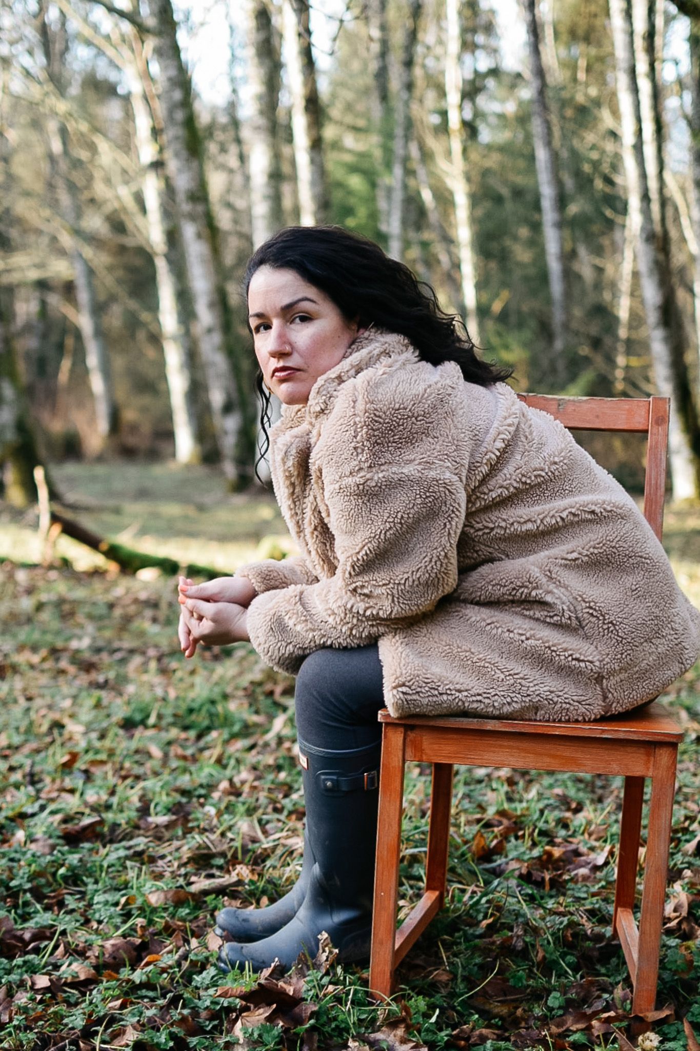 Person in cozy fleece jacket sitting on wooden bench in forest setting.