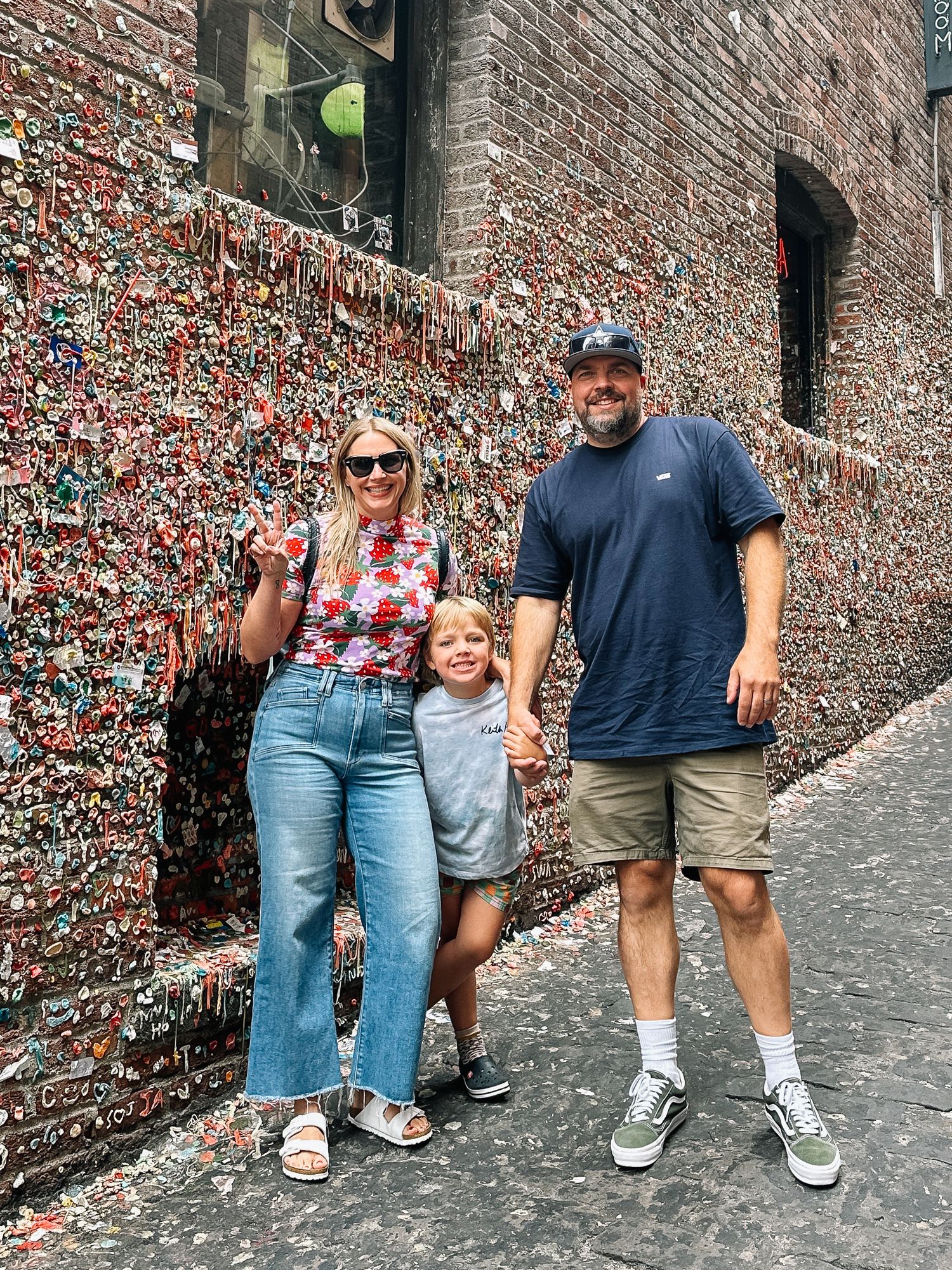 Family poses together against brick wall covered in colorful notes and decorations.