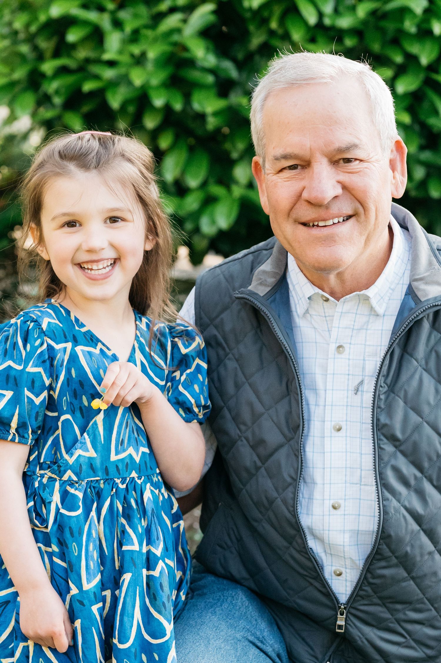 Outdoor family portrait in a garden setting with blue patterned dress and casual attire.