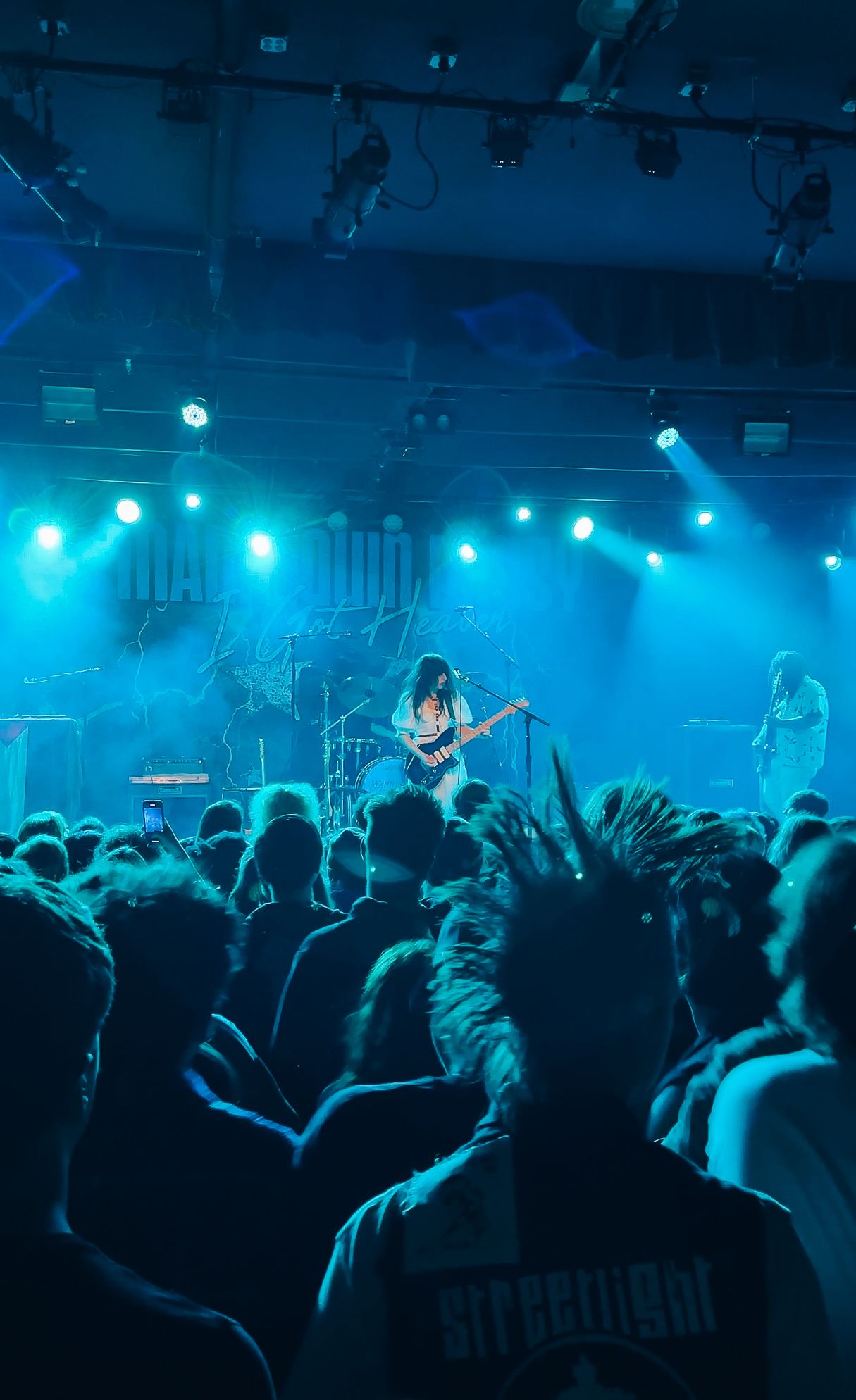 Concert crowd silhouetted against blue stage lighting at a live music performance.