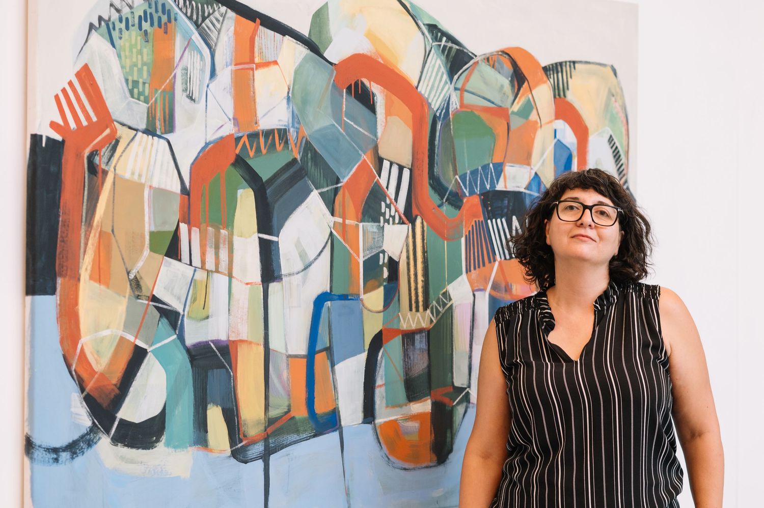 Abstract colorful artwork hangs on gallery wall with viewer observing the geometric patterns.