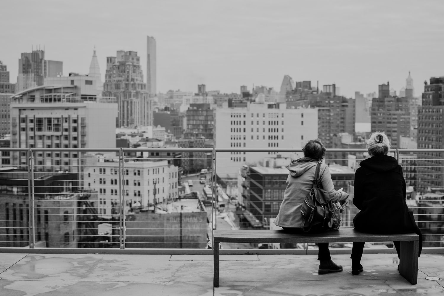Black and white photo of people sitting on a rooftop overlooking a city skyline.
