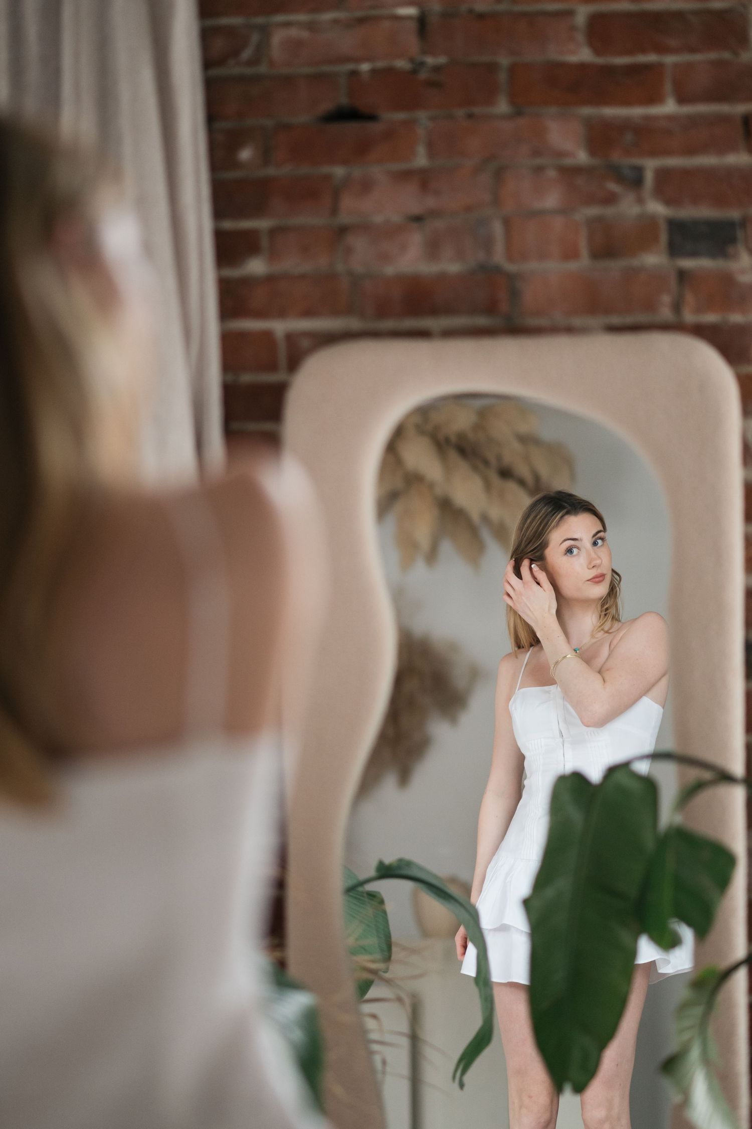 Indoor portraits with person in white tank top near brick wall and green plants.