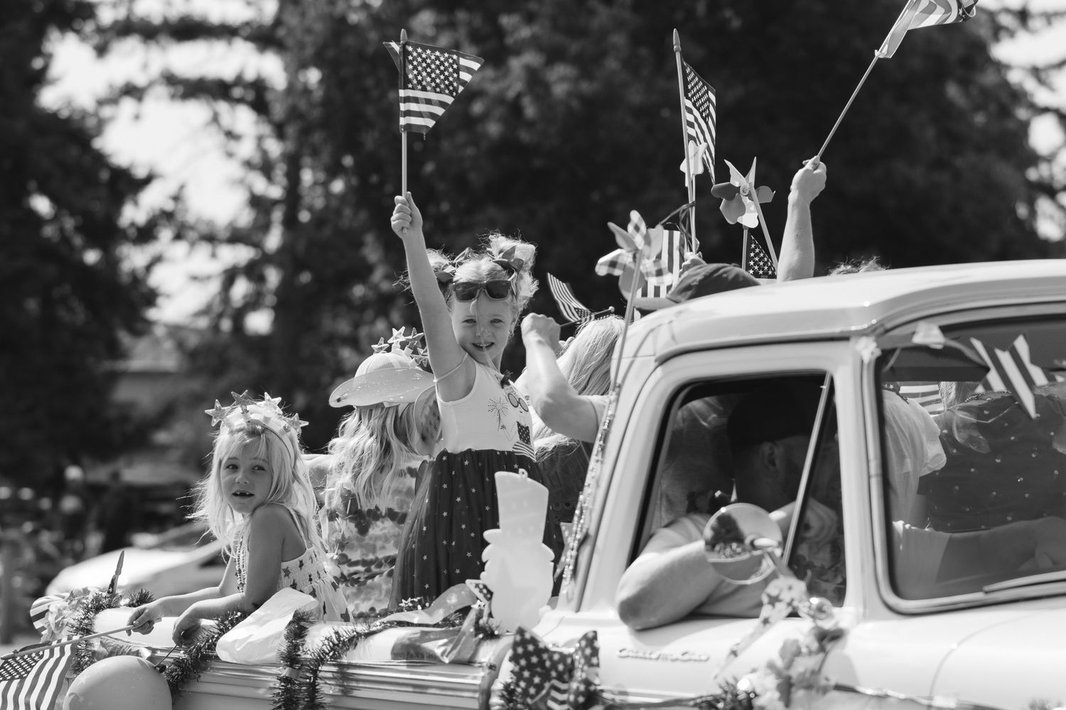 Black and white vintage photo of decorated cars in a parade with American flags.