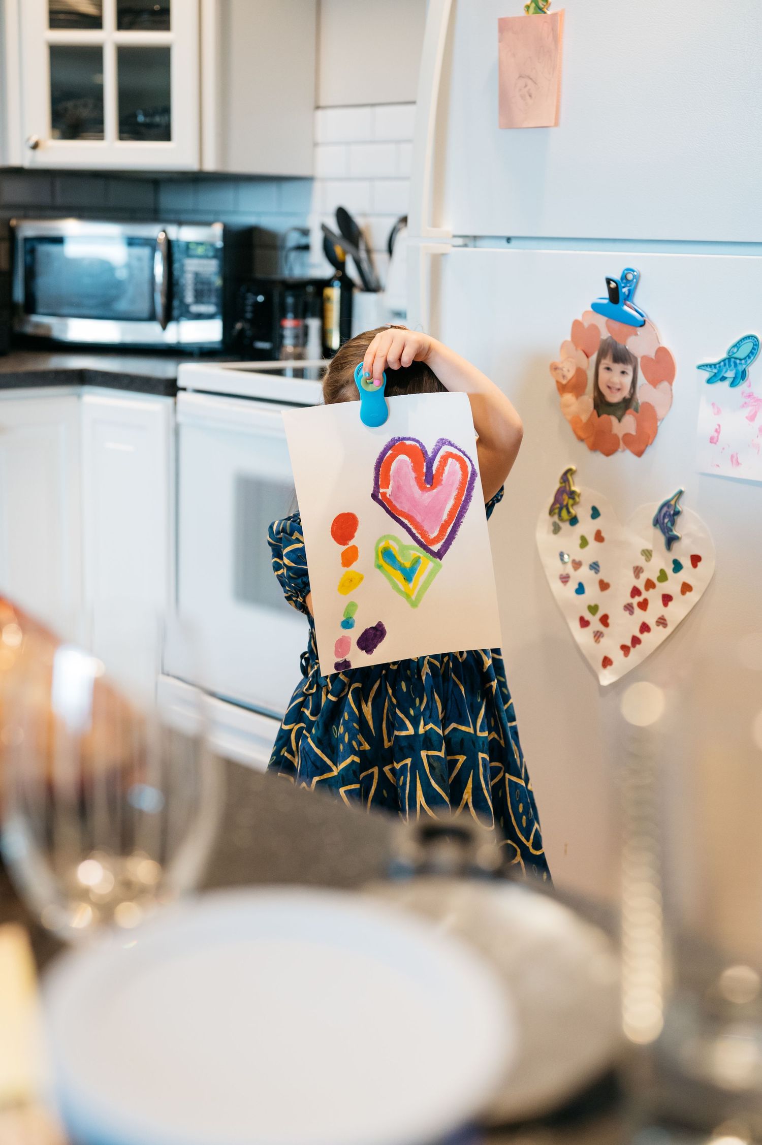 Colorful children's artwork and hearts displayed on string in a bright white kitchen.