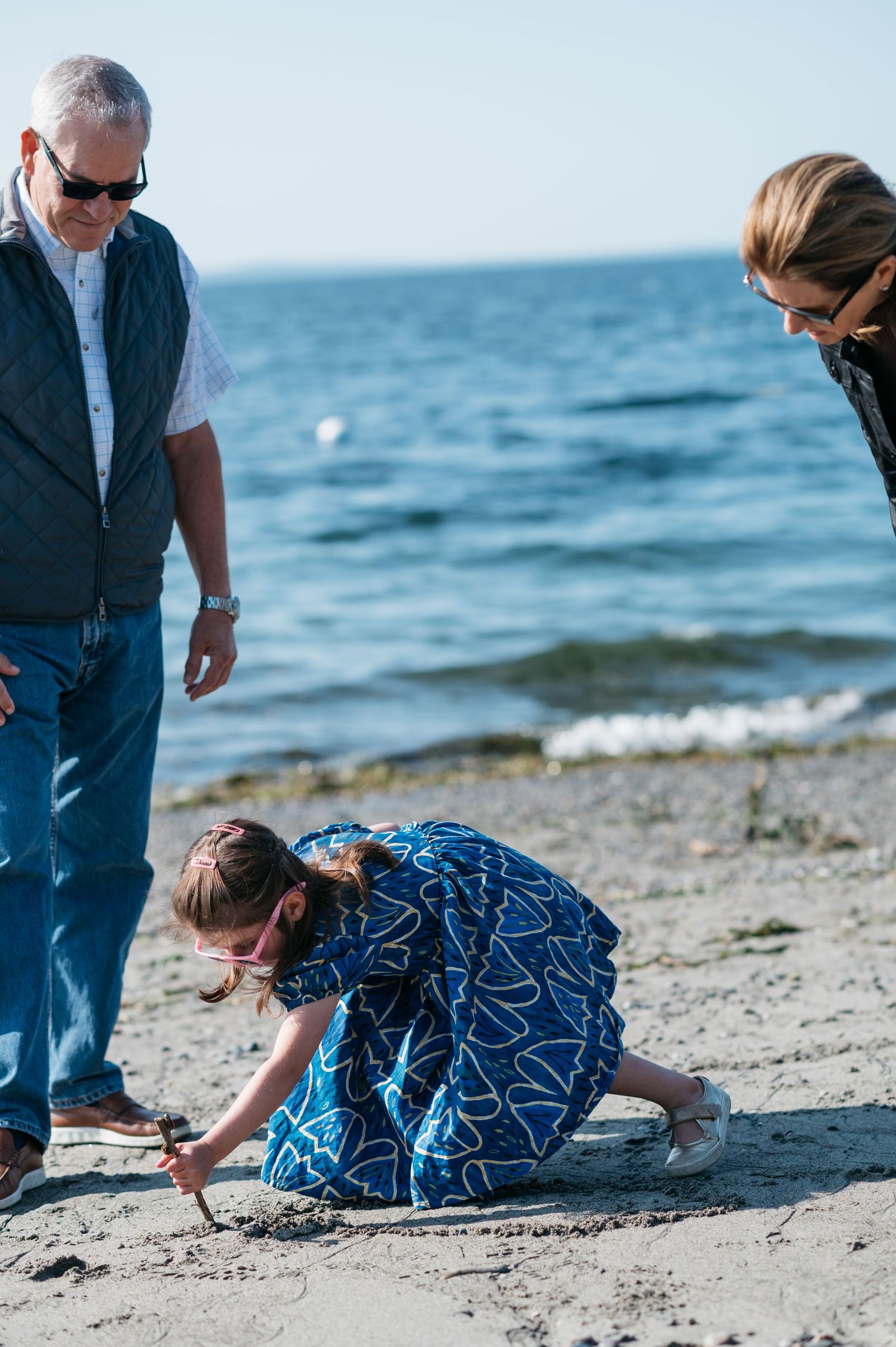 People exploring and collecting items on a rocky beach by the ocean on a sunny day.