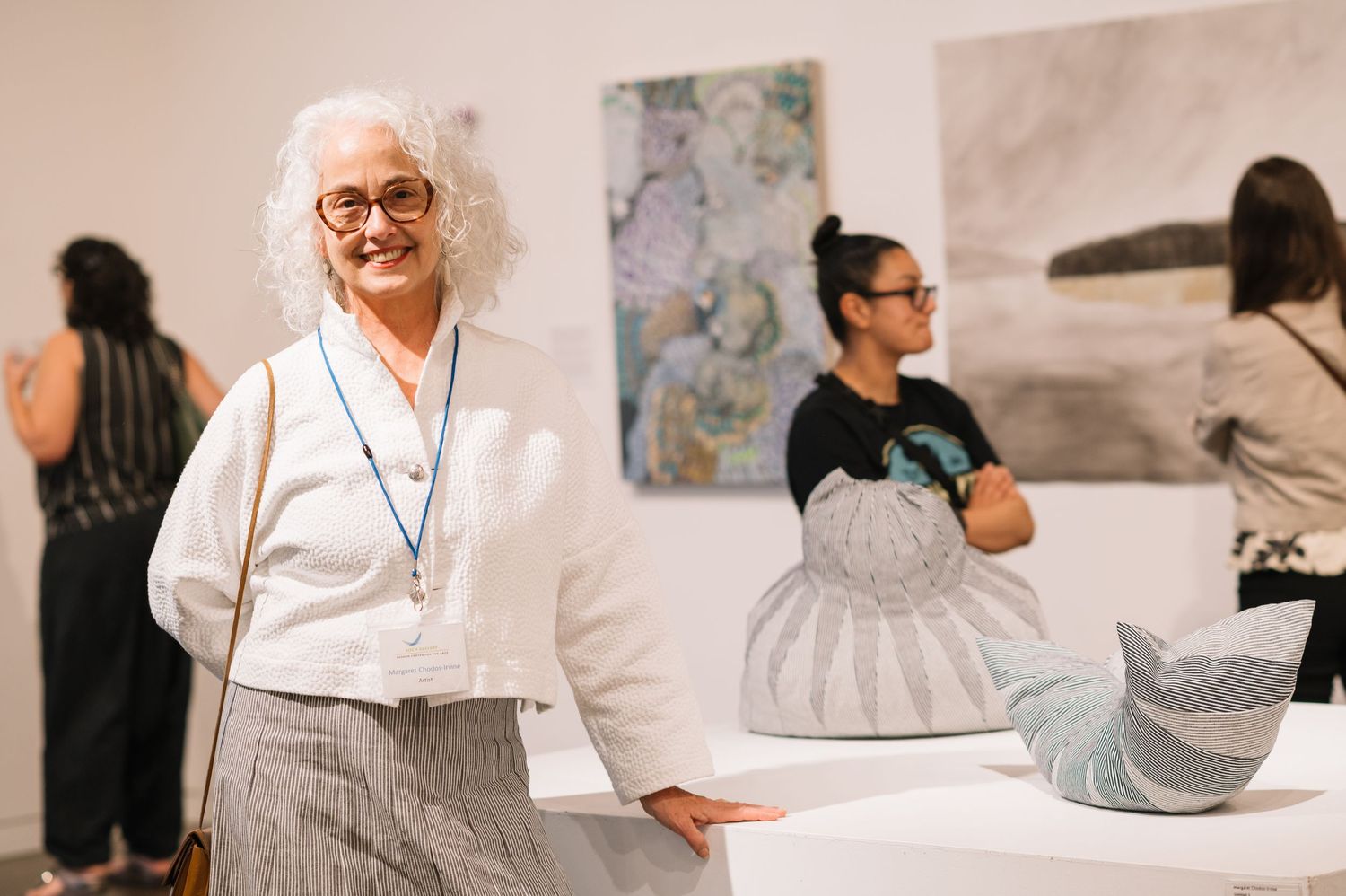 Museum visitors examine artwork displays in a bright gallery setting with white walls.
