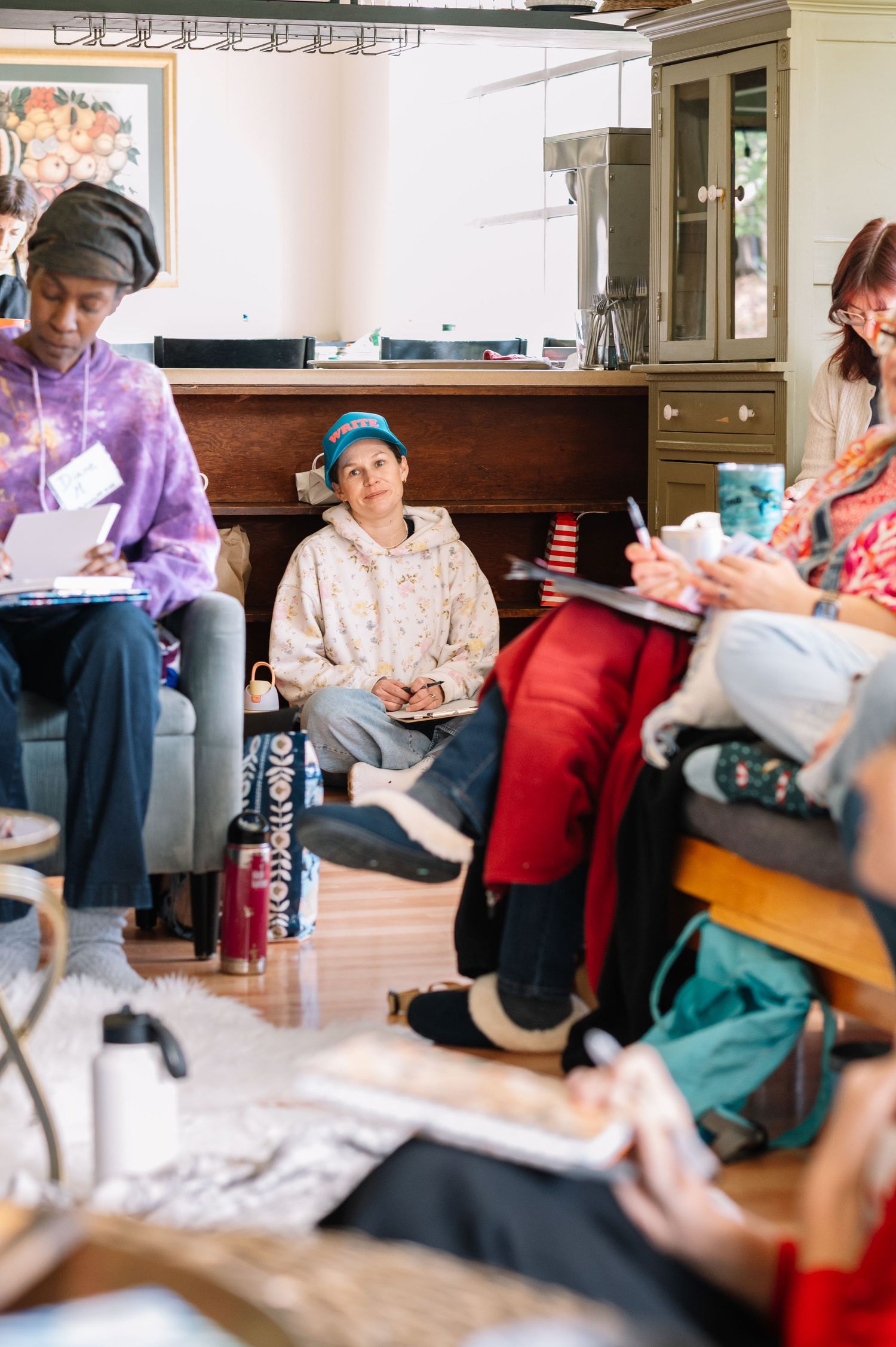 Group of people sitting in a circle during an indoor workshop, taking notes and listening attentively in a cozy home setting.